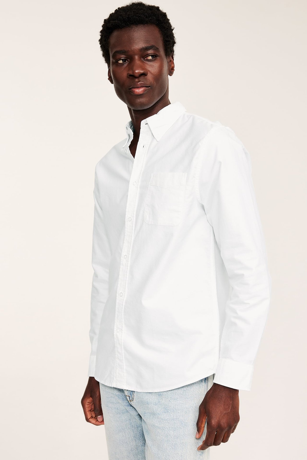 Frontvy av man i vit regular fit oxfordskjorta med button-down krage och ljusblå jeans.