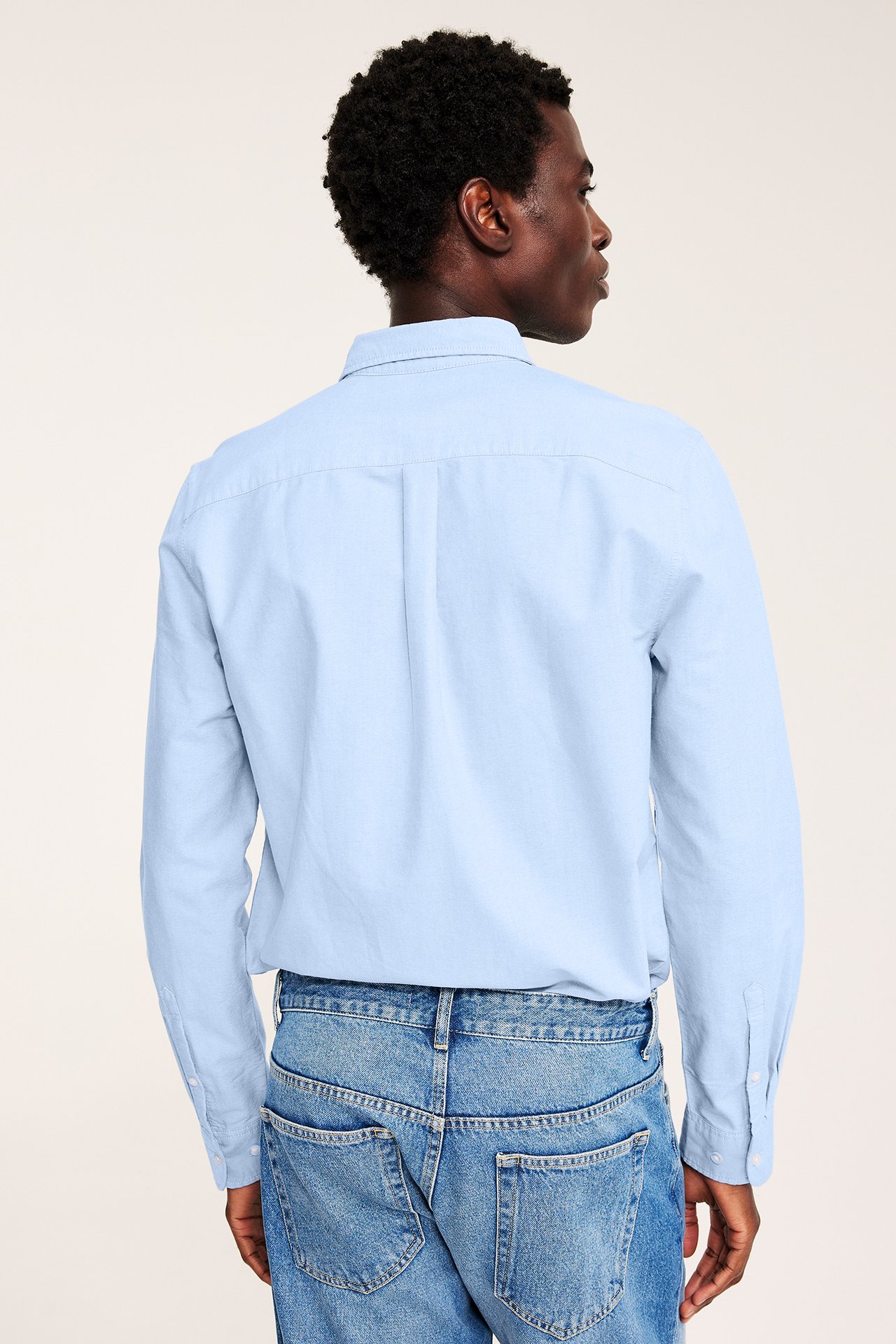 Bakside av mannlig modell iført lyseblå langermet skjorte og blå jeans.