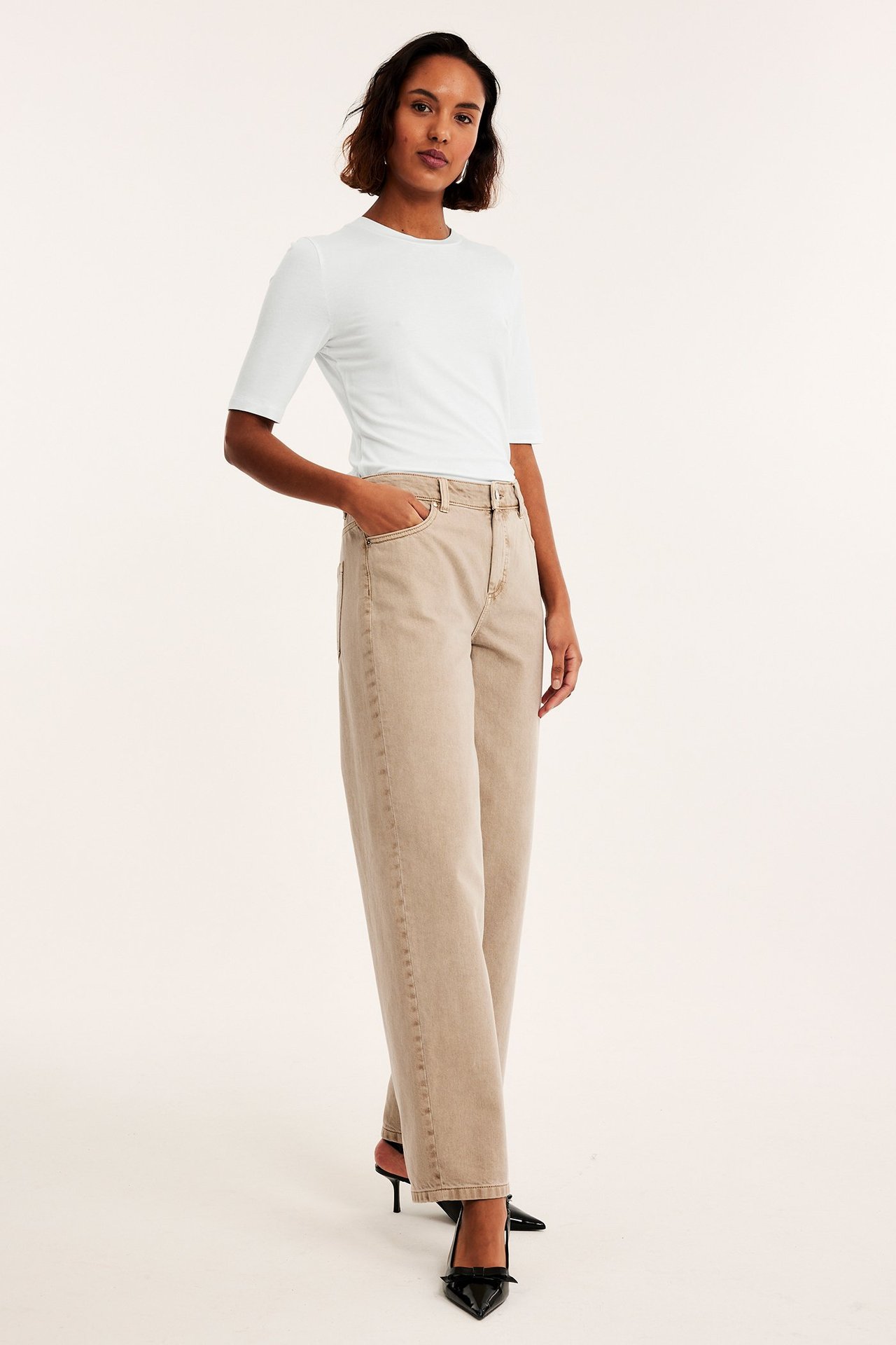 Front: kvinne i et offwhite ettersittende t-skjorte, beige vide jeans og svarte hæler.