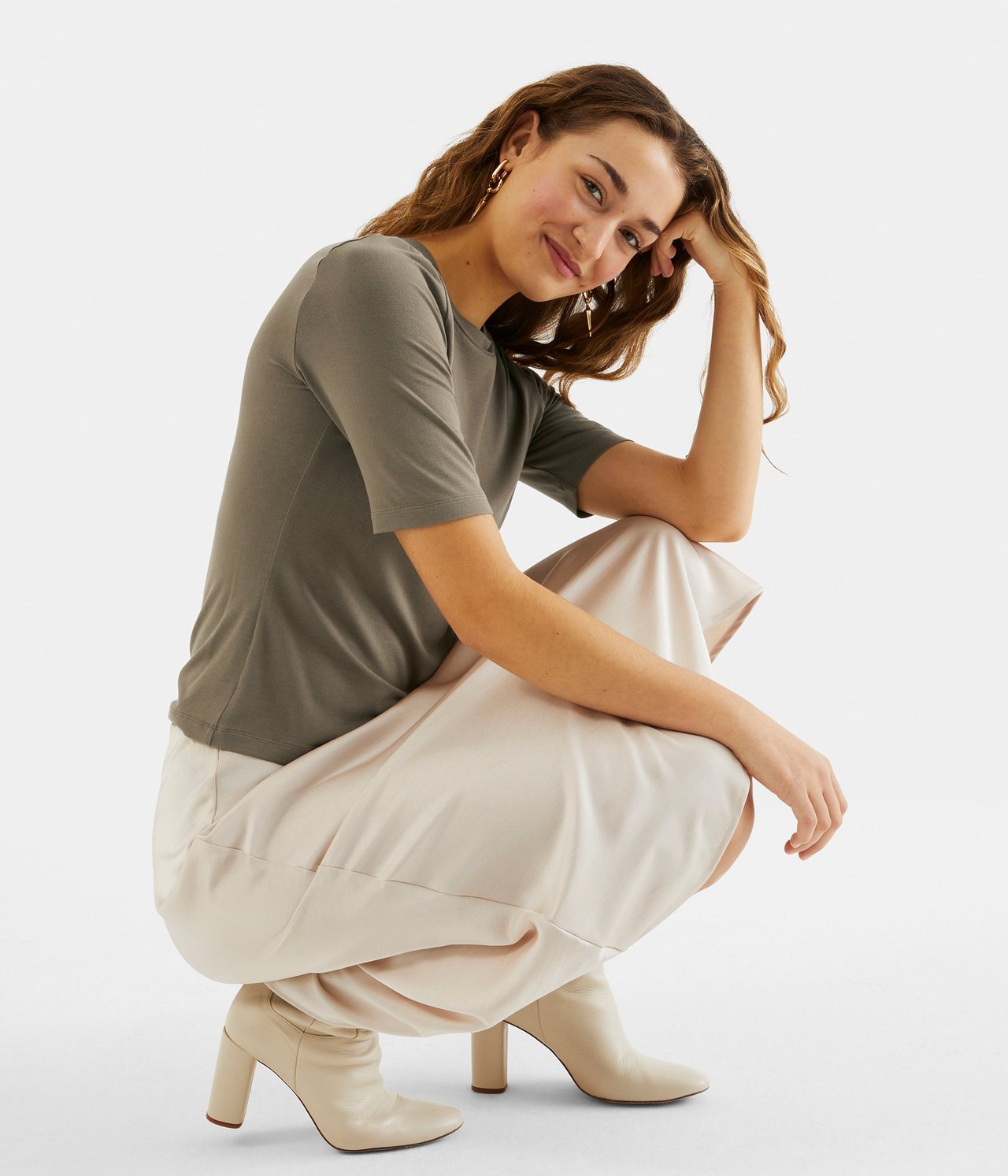 Forfra: Kvinne i tettsittende brun kortermet t-skjorte, lyst beige skjørt og beige ankelstøvler.