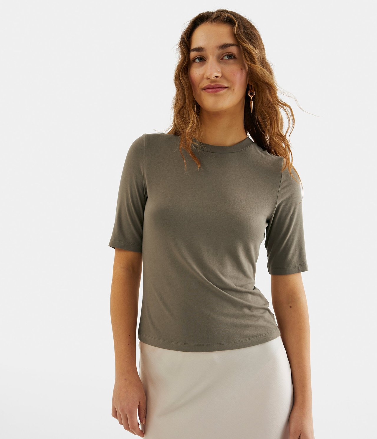 Forfra: Kvinne i en tettsittende, kortermet brun t-skjorte og et lyst skjørt.