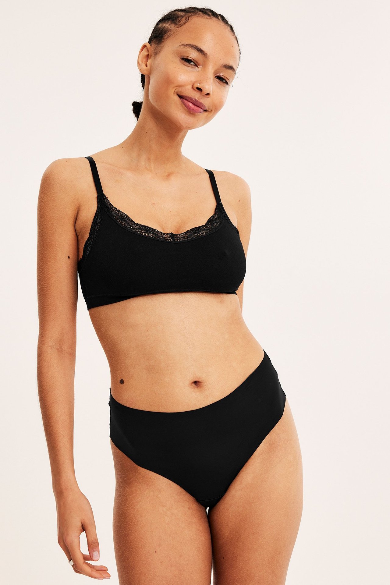 Forfra, kvinne i svart clean-cut midi stringtruse og matchende svart bralette med blondekant.