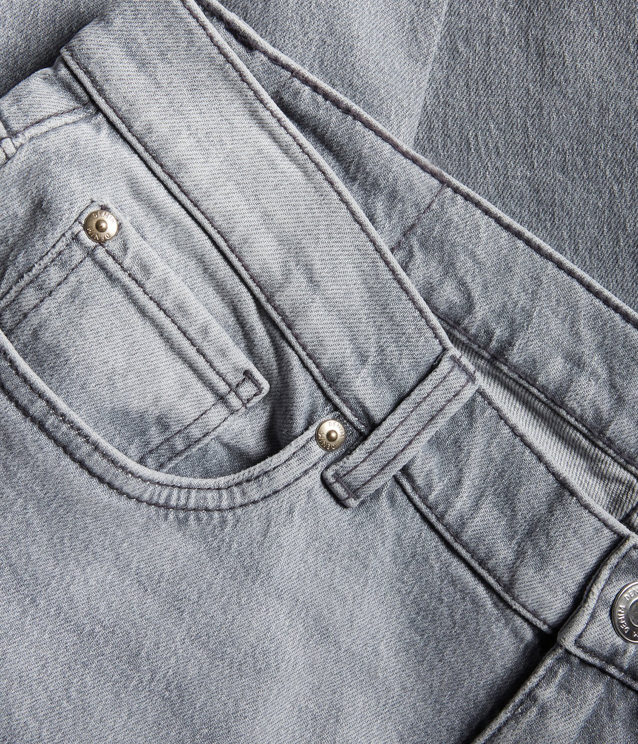 Nærbilde forfra av lysegrå regular fit jeans i denim med gullfargede nagler og en frontlomme.