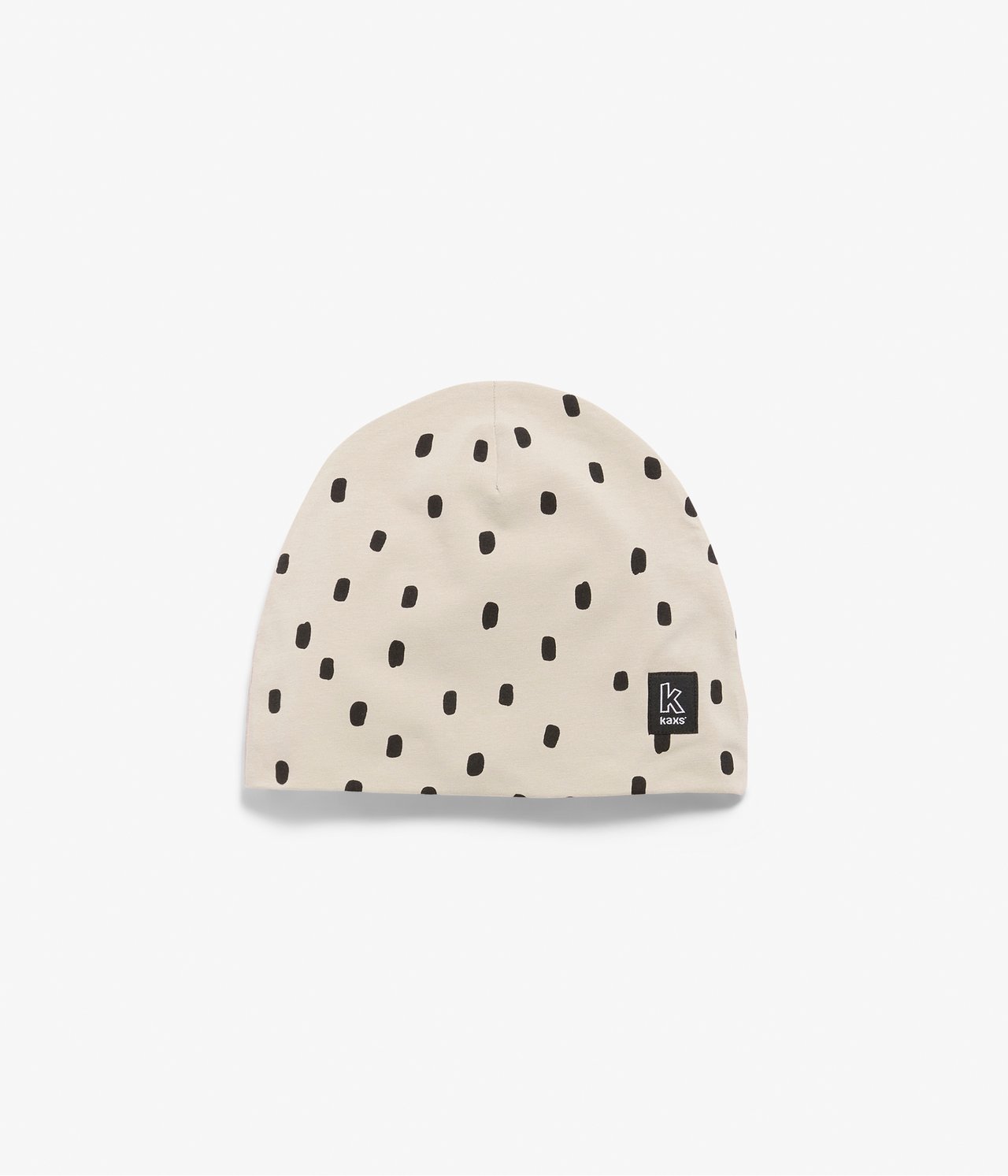 Edestä: Lasten beige trikoopipo mustalla epäsäännöllisellä pilkkukuviolla.