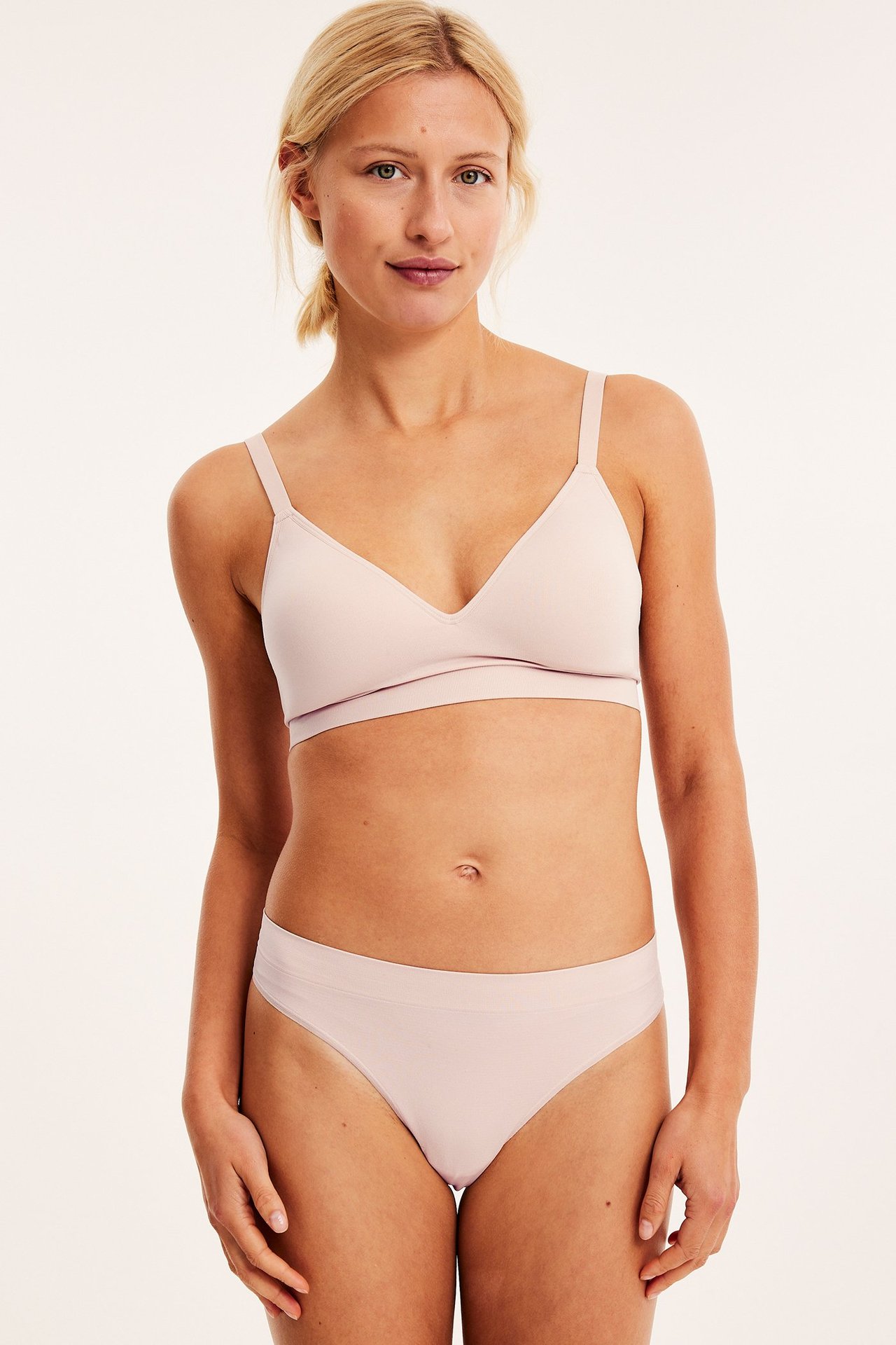 Framifrån, kvinna i ljusrosa sömlös stringtrosa och matchande ljusrosa sömlös BH.