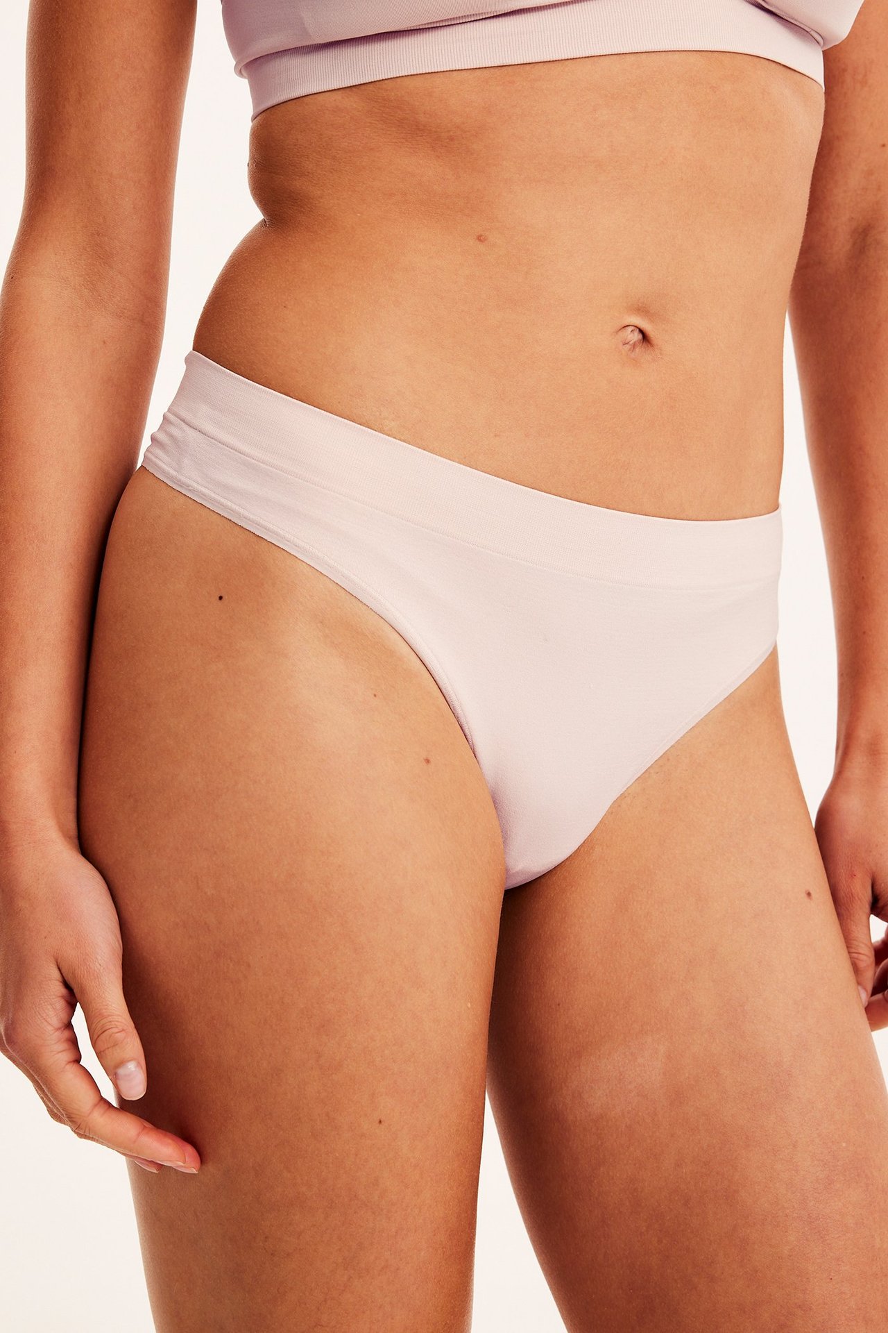 Nærbilde av en kvinne i en lys rosa sømløs stringtruse og en matchende sømløs BH.