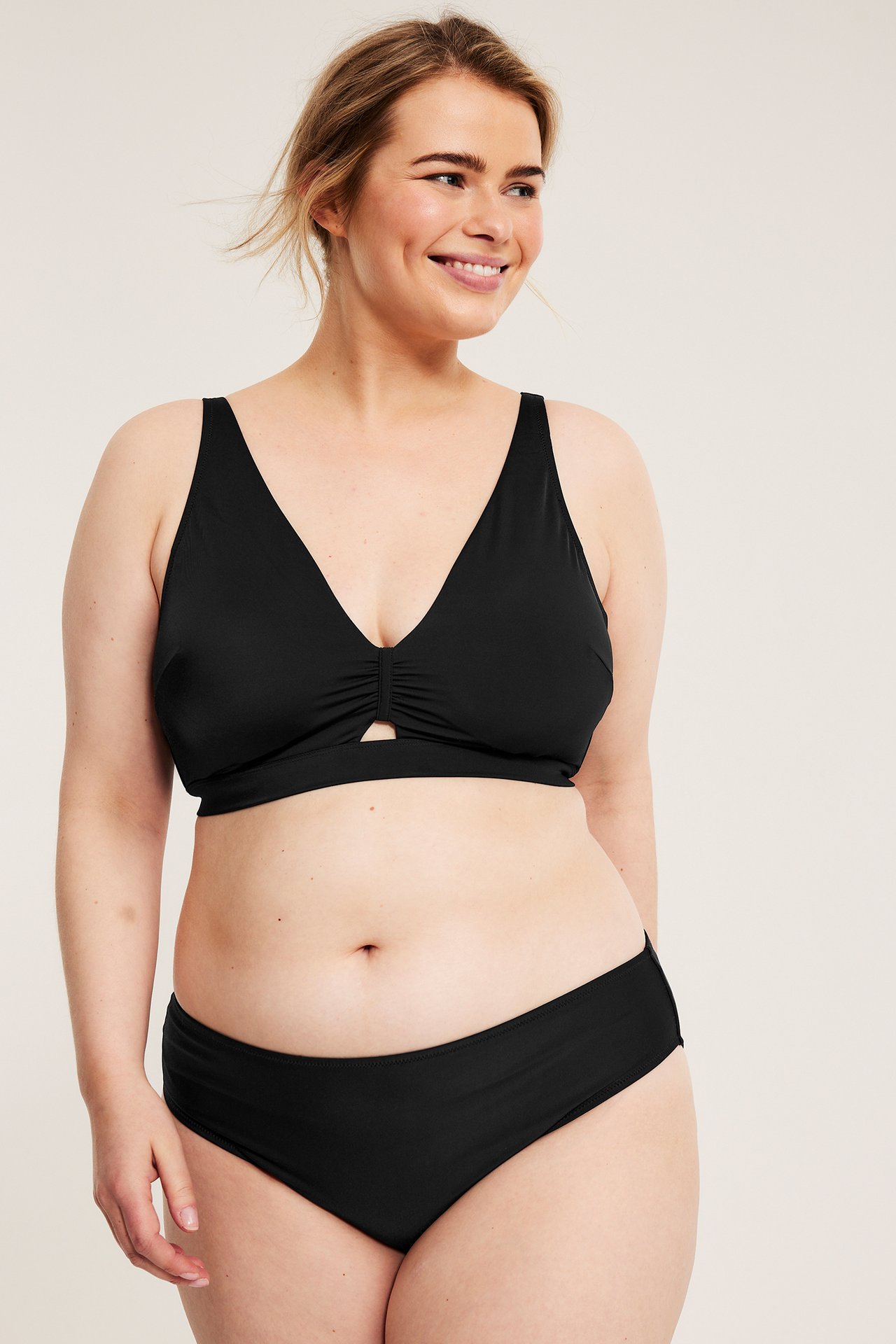 Frontbilde: En kvinne har på seg en svart polstret bikinitopp med rynker og cut-out, samt matchende truse.