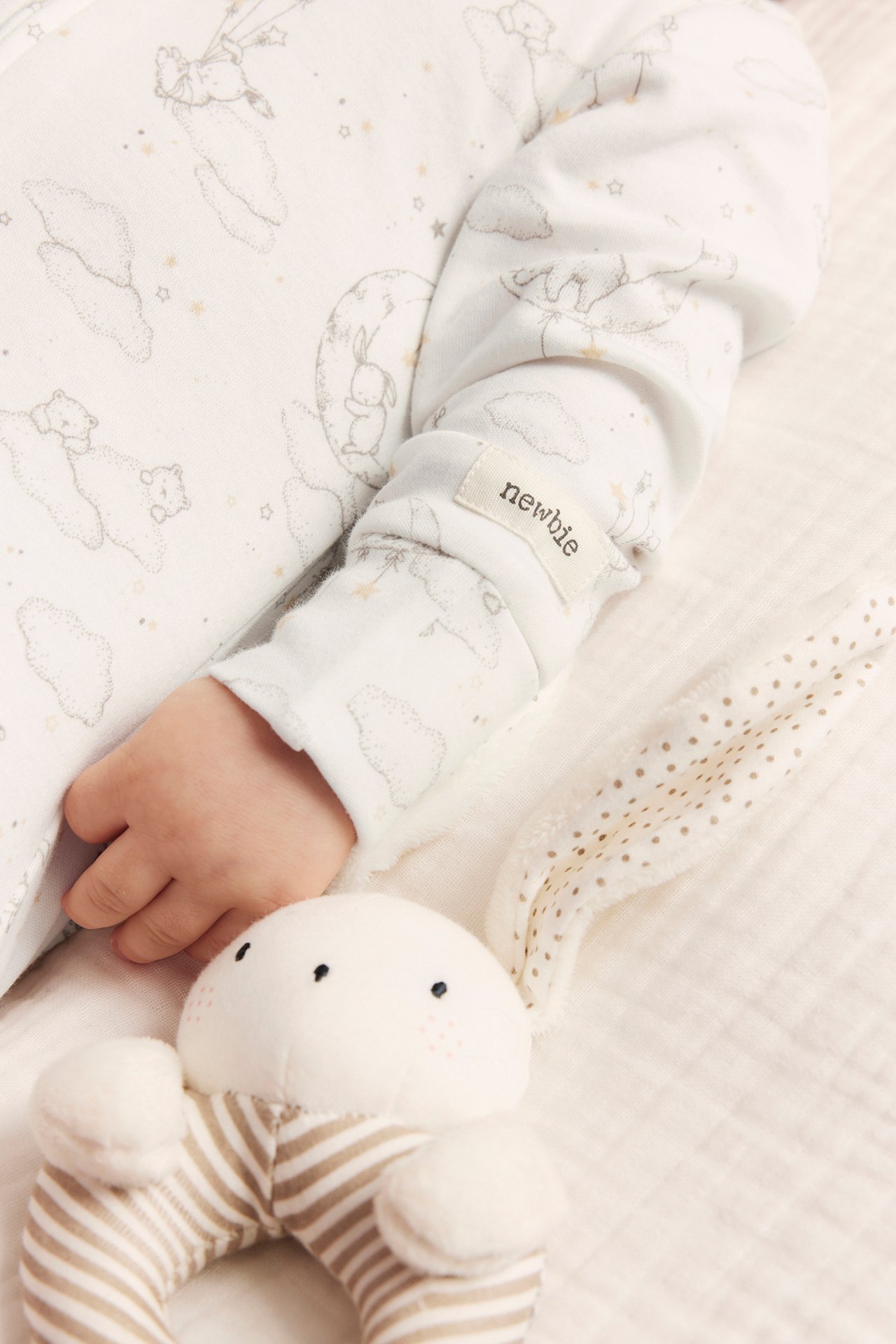 Lähikuva vauvan kädestä offwhite-puuvillapyjamassa eläinkuviolla, kaninhelistimen vieressä.