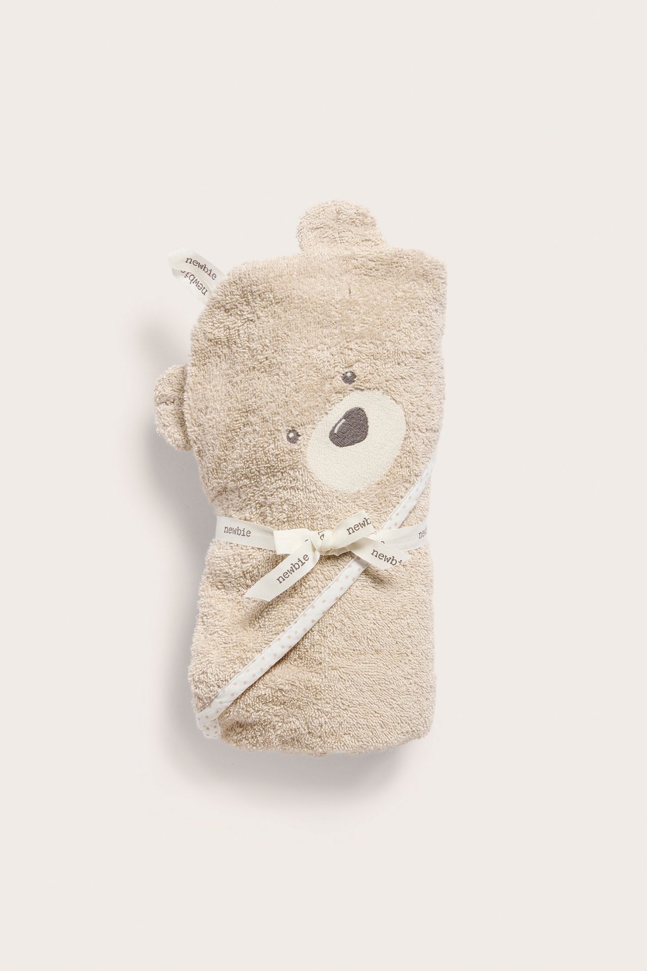 Frontvy: Beige frottéhandduk med huva för baby, vikt, med björnöron, broderat ansikte, knuten med band.