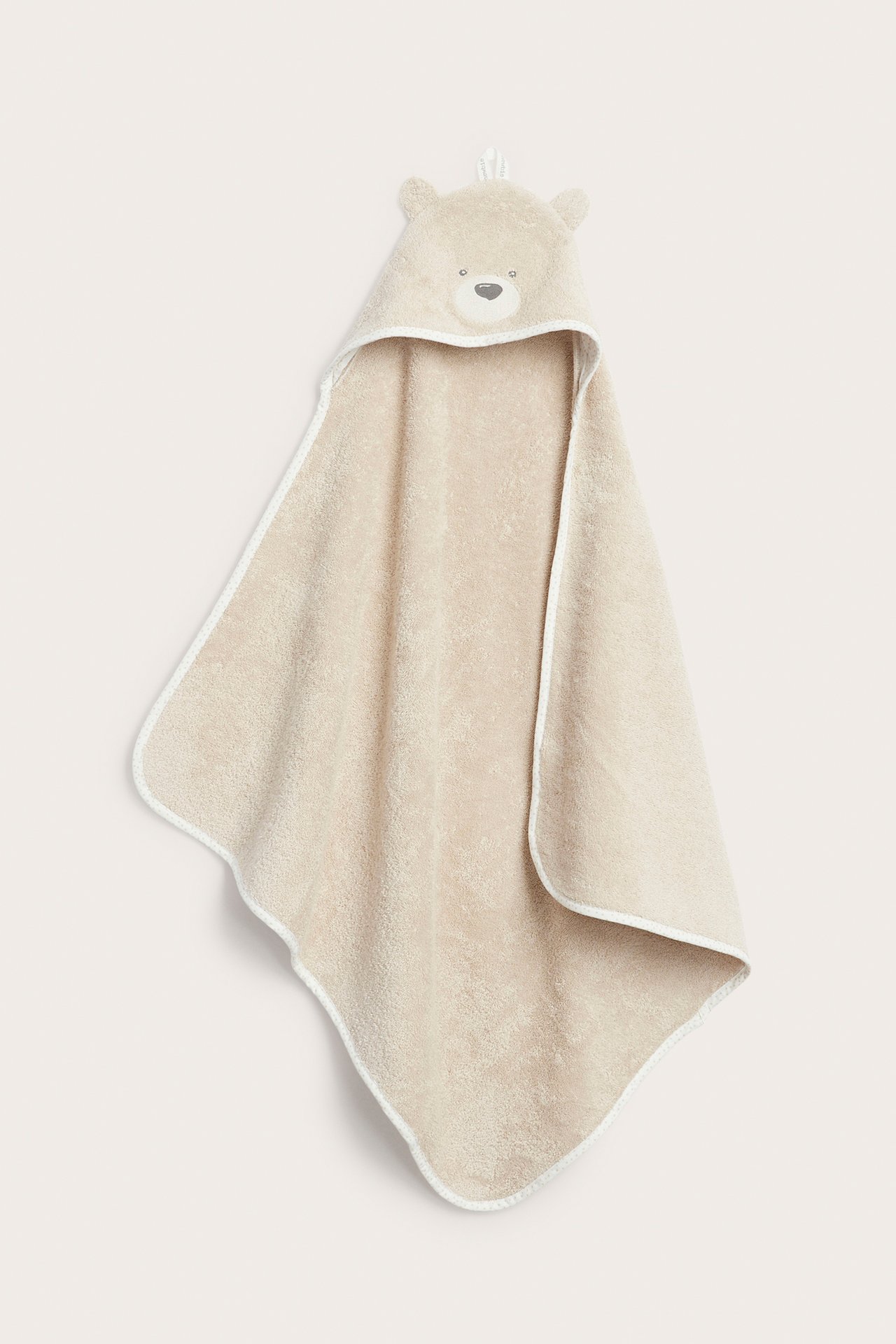 Framifrån: beige frottéhandduk med huva för baby, med björnöron och broderat ansikte.