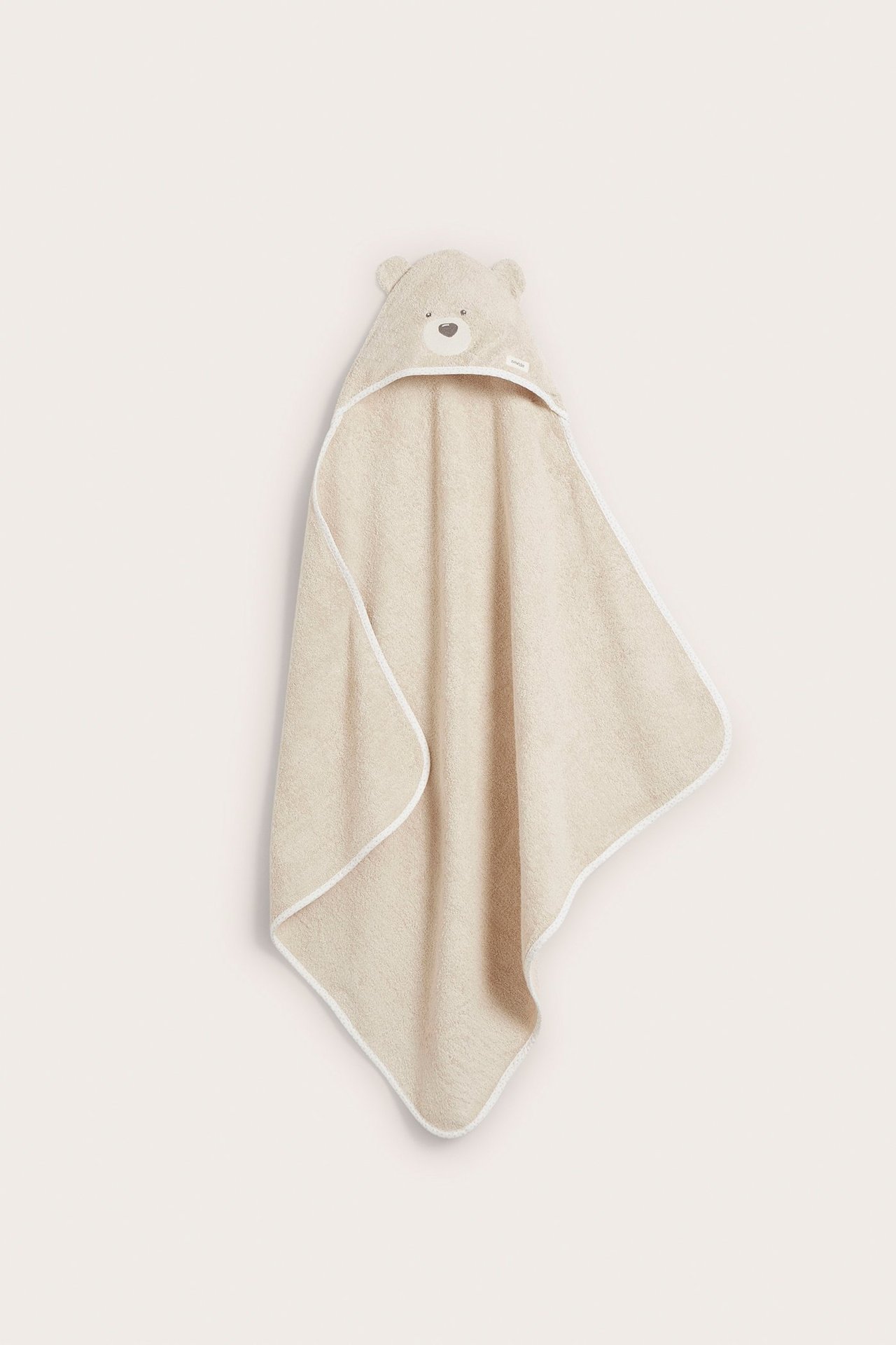 Frontvy av en beige frottéhandduk med huva för baby, med björnöron och broderade ansiktsdetaljer.