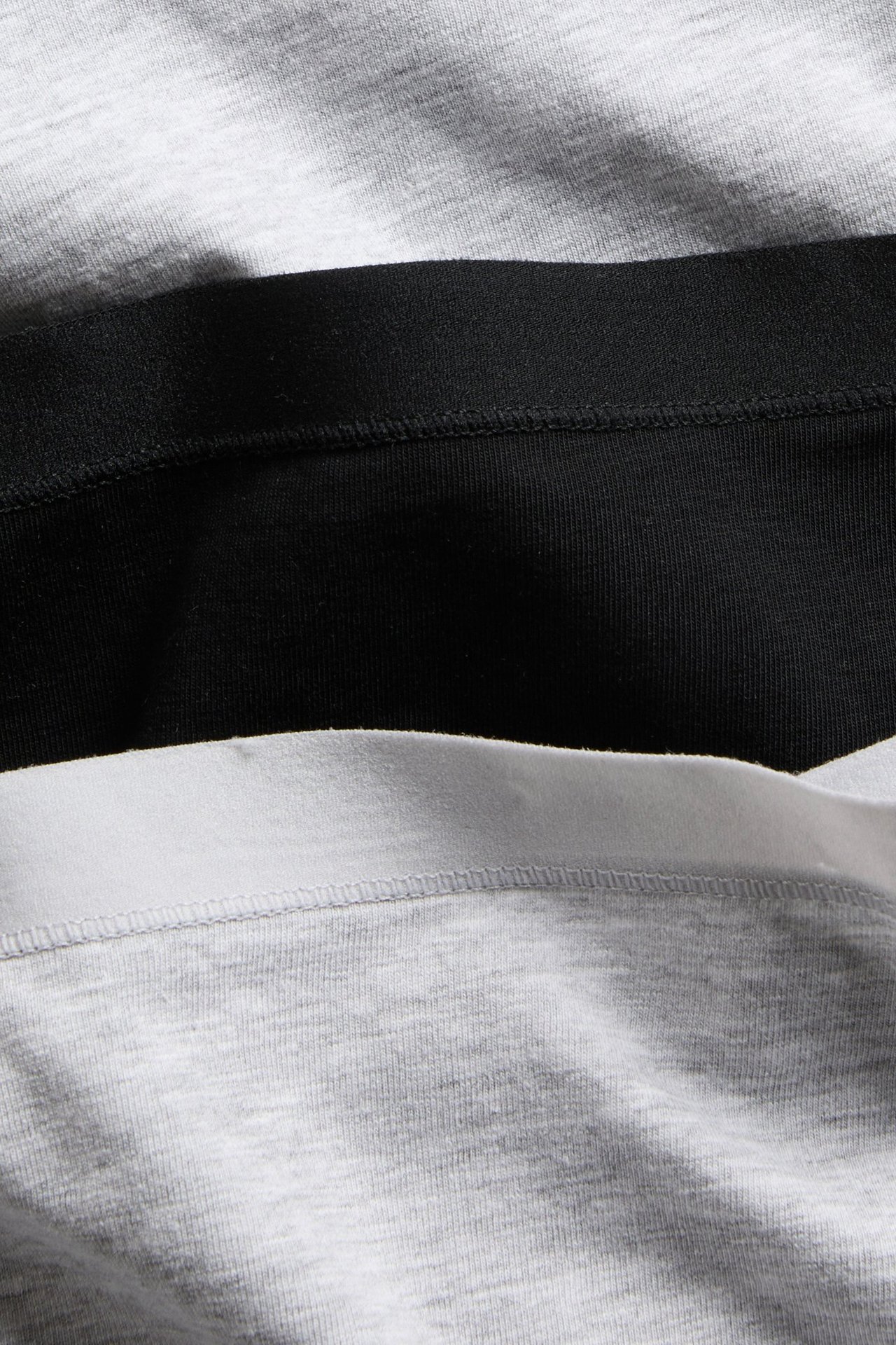 Nærbilde av stablede damebokserundertrøyer i bomull: gråmelert, svart og grå med hvit linning.