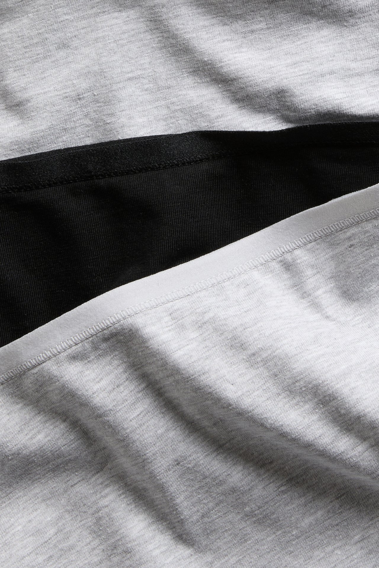 Närbild av ett 3-pack bomullstrosor i gråmelerat, svart och ljusgrått/vitt.