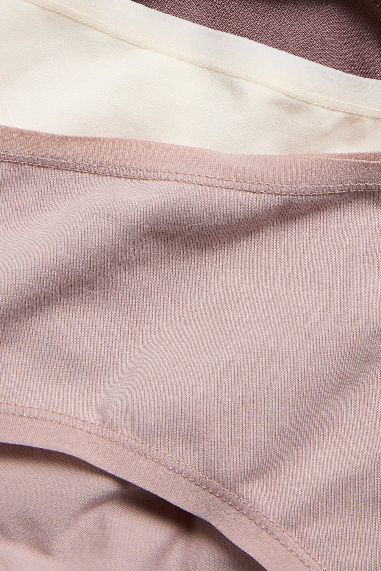 Zbliżenie trzech ułożonych damskich majtek bawełnianych w kolorach jasnoróżowym, ecru i ciemnofioletowym.