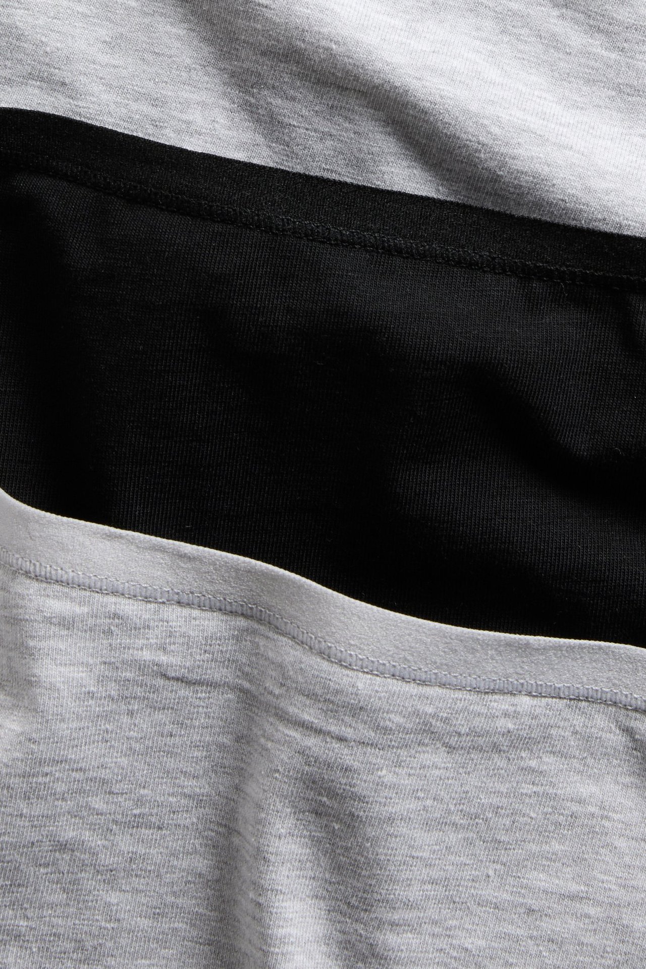 Närbild av tre vikta höga dambrieftrosor: två ljusgråmelerade och en svart bomullstrosa.