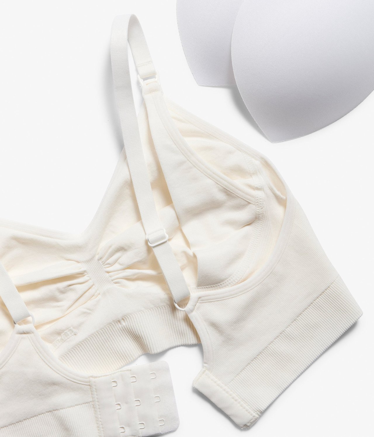 Widok z góry na biały, bezszwowy biustonosz do karmienia z regulowanymi ramiączkami, zapięciem i wyjmowanymi wkładkami.