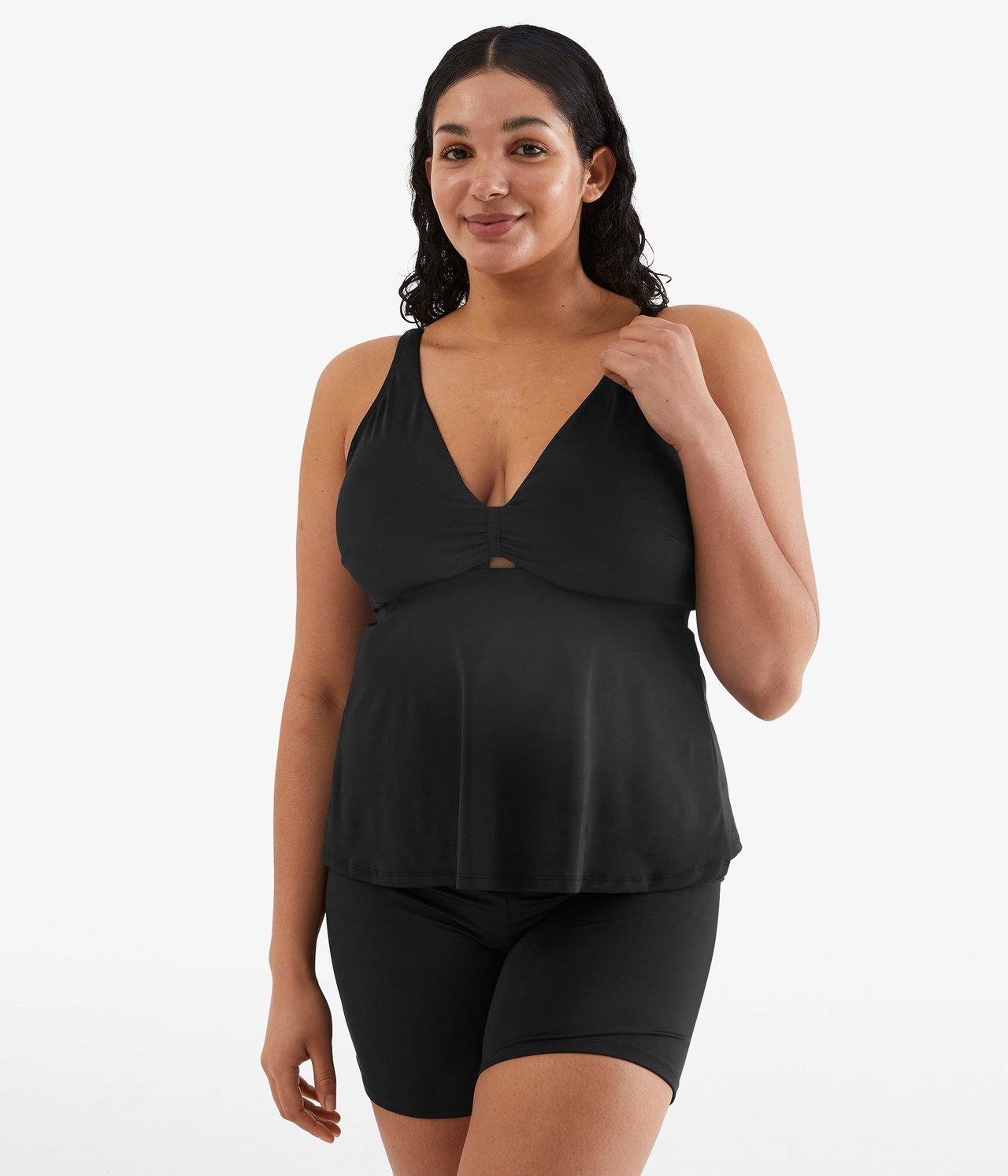 Widok z przodu kobiety w czarnym topie tankini z marszczonym wycięciem i czarnych szortach bikini.