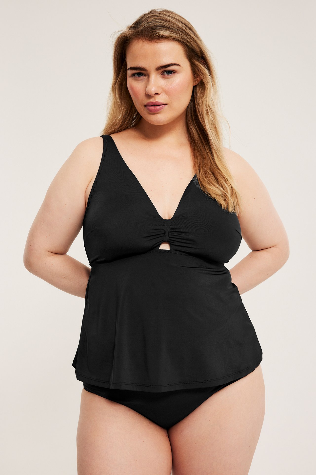 Naisen etukuva, musta tankini-bikinitoppi V-pääntiellä, rypytetyllä leikkauksella ja yhteensopivilla alaosilla.