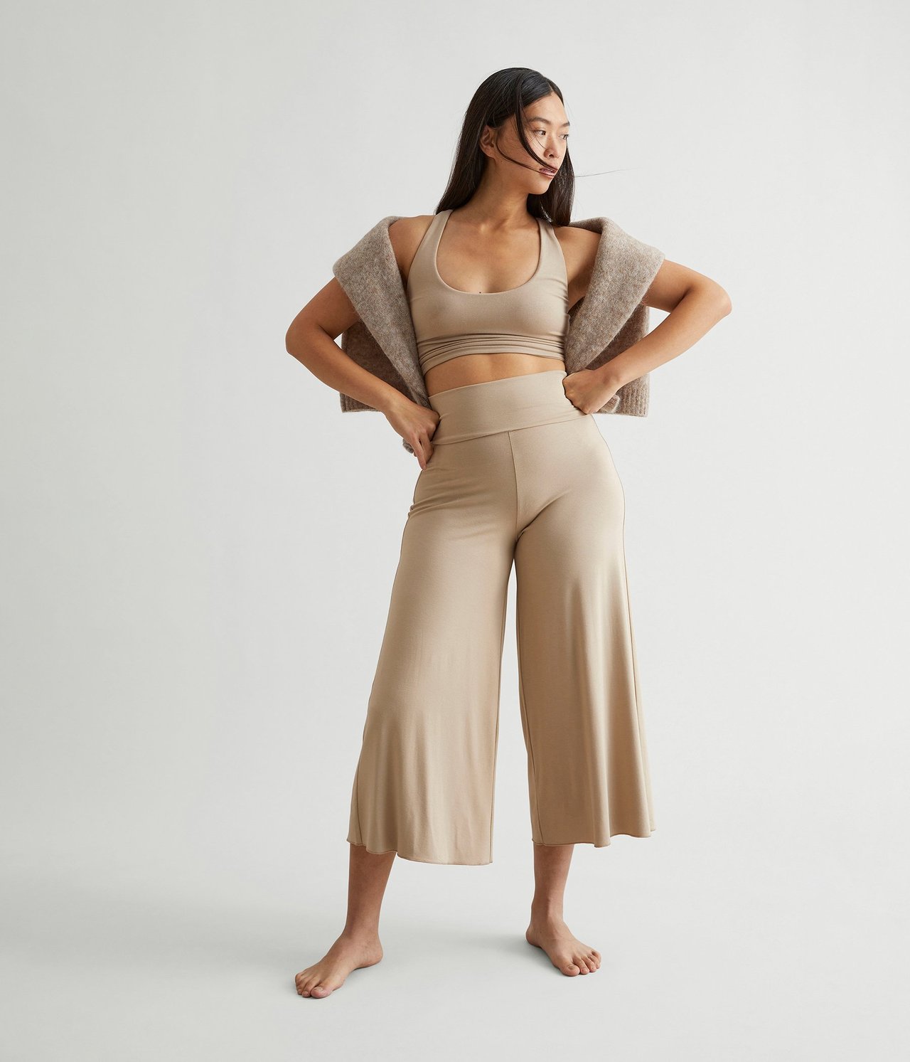 Frontvisning: Kvinne i beige vide loungebukser, matchende crop top og en drapert strikket cardigan.