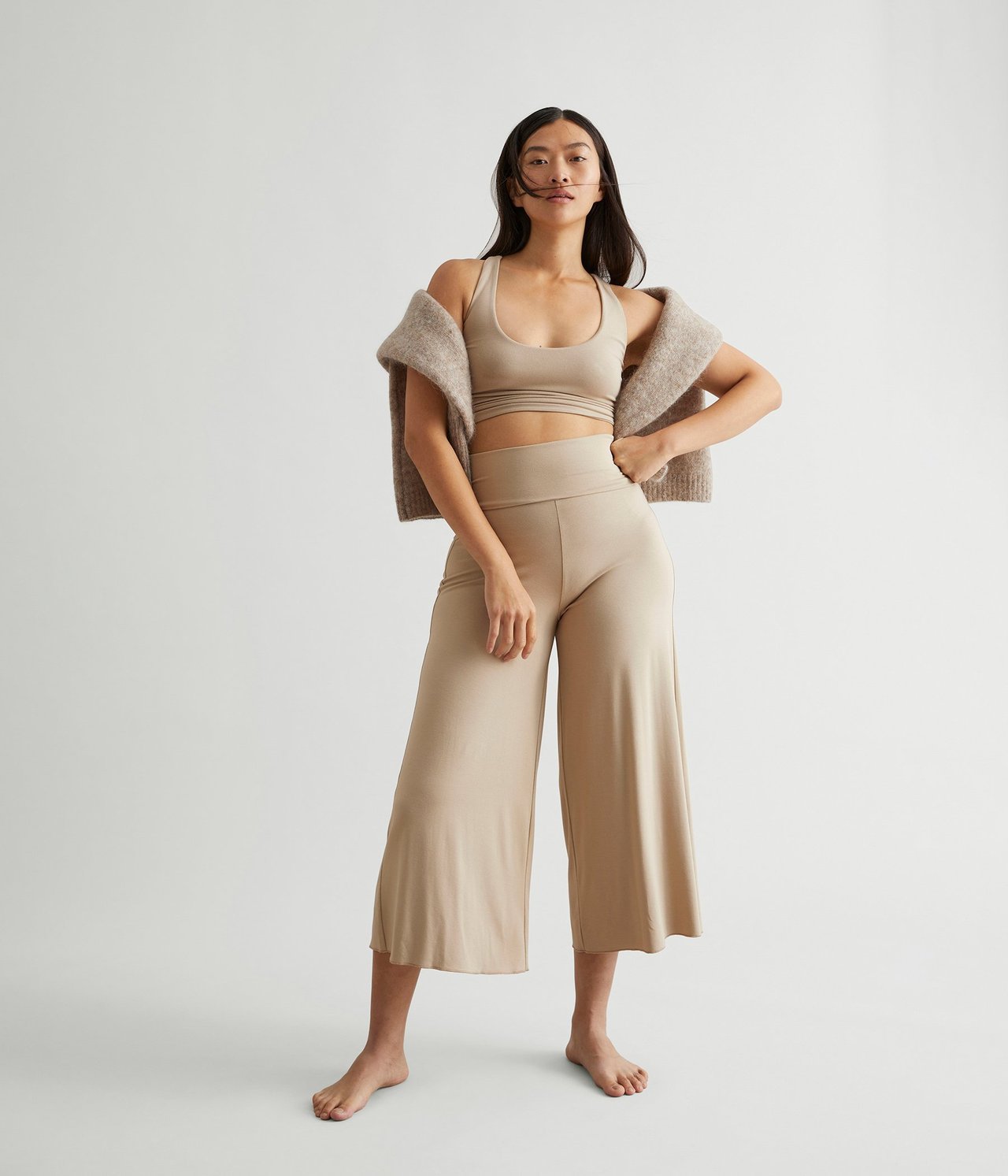 Forfra: kvinne i beige vide loungewear-bukser, matchende crop top og strikket cardigan.
