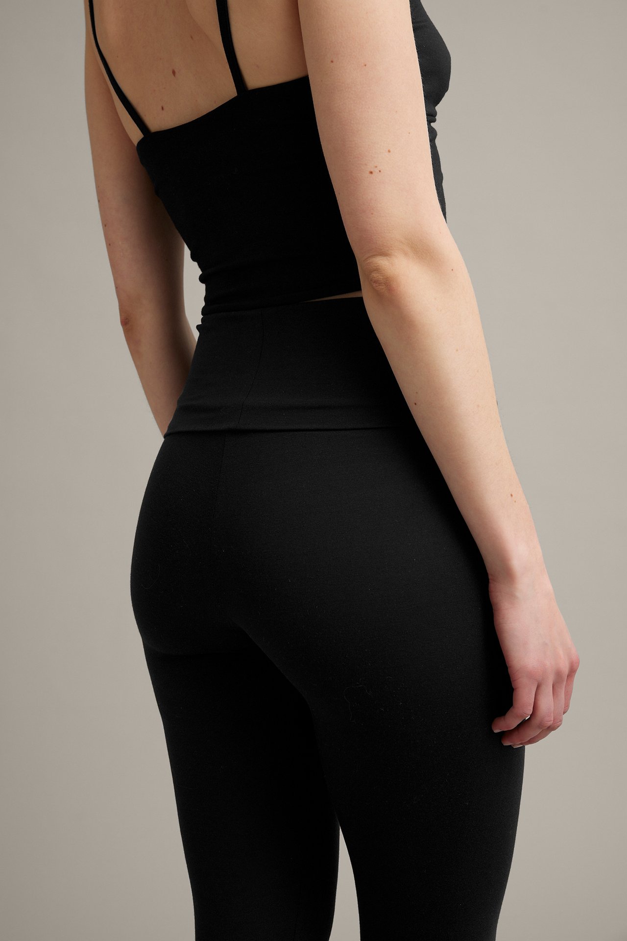 Ryggvy av en kvinna i svarta högmidjade leggings och ett svart linne.