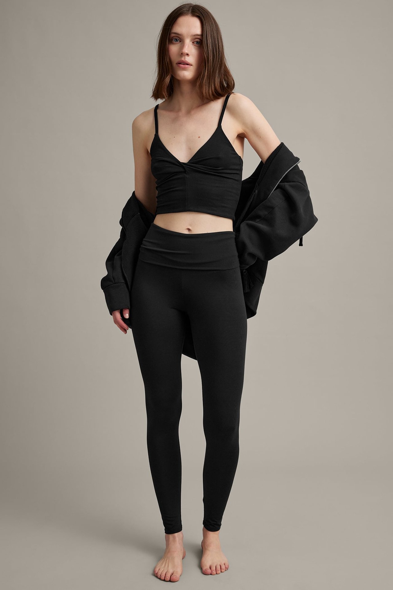 Frontbilde av en kvinne i svarte leggings, en svart crop top og en svart hettegenser.