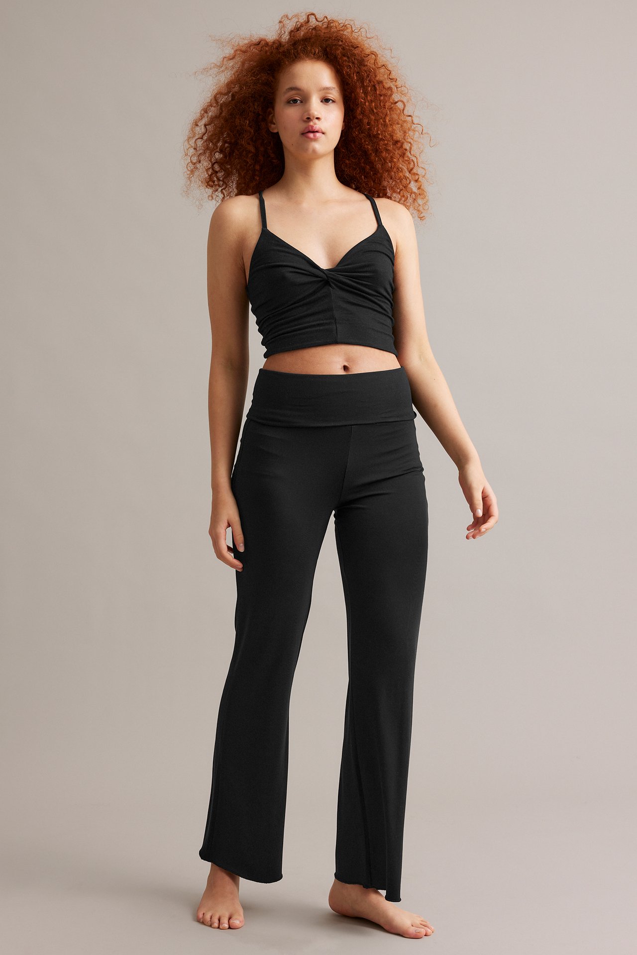 Kobieta z przodu w czarnych spodniach dresowych typu bootcut i pasującym skręconym crop topie.