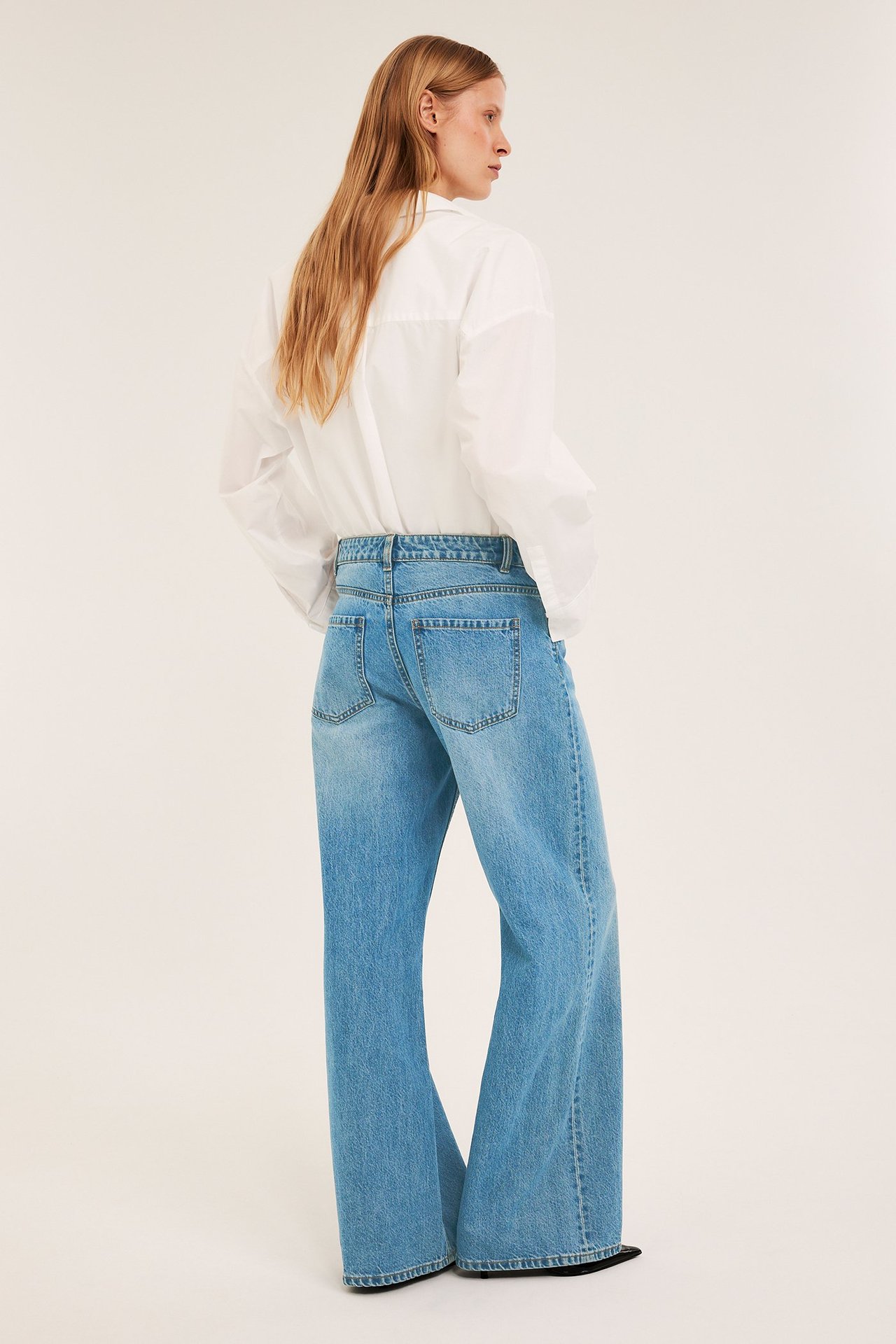 Takakuva naisesta yllään vaaleansiniset leveälahkeiset, korkeavyötäröiset farkut ja valkoinen paita.