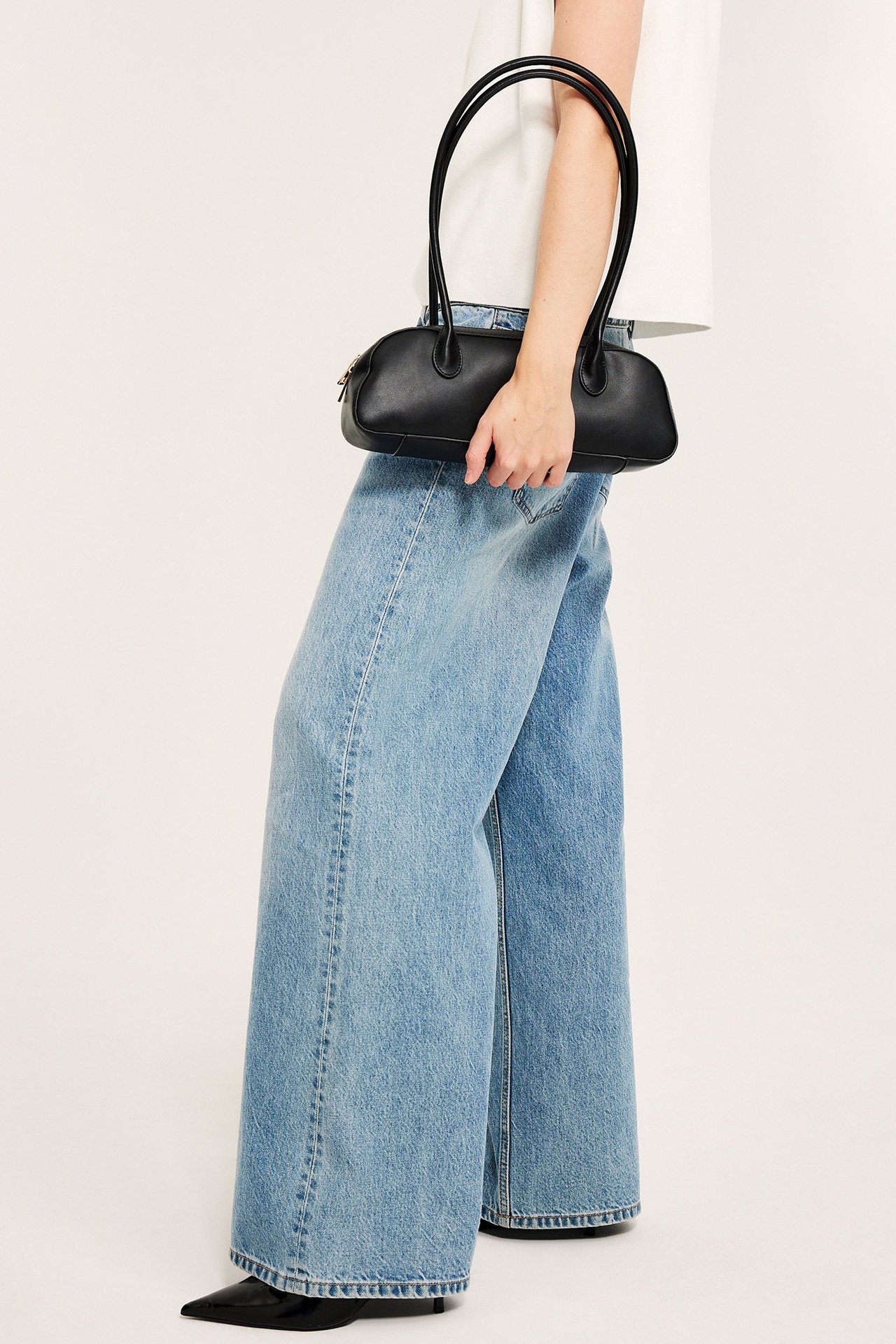 Sidebilde av en kvinne i lyseblå vide high-waist denimjeans, hvit topp, holder sort håndveske.