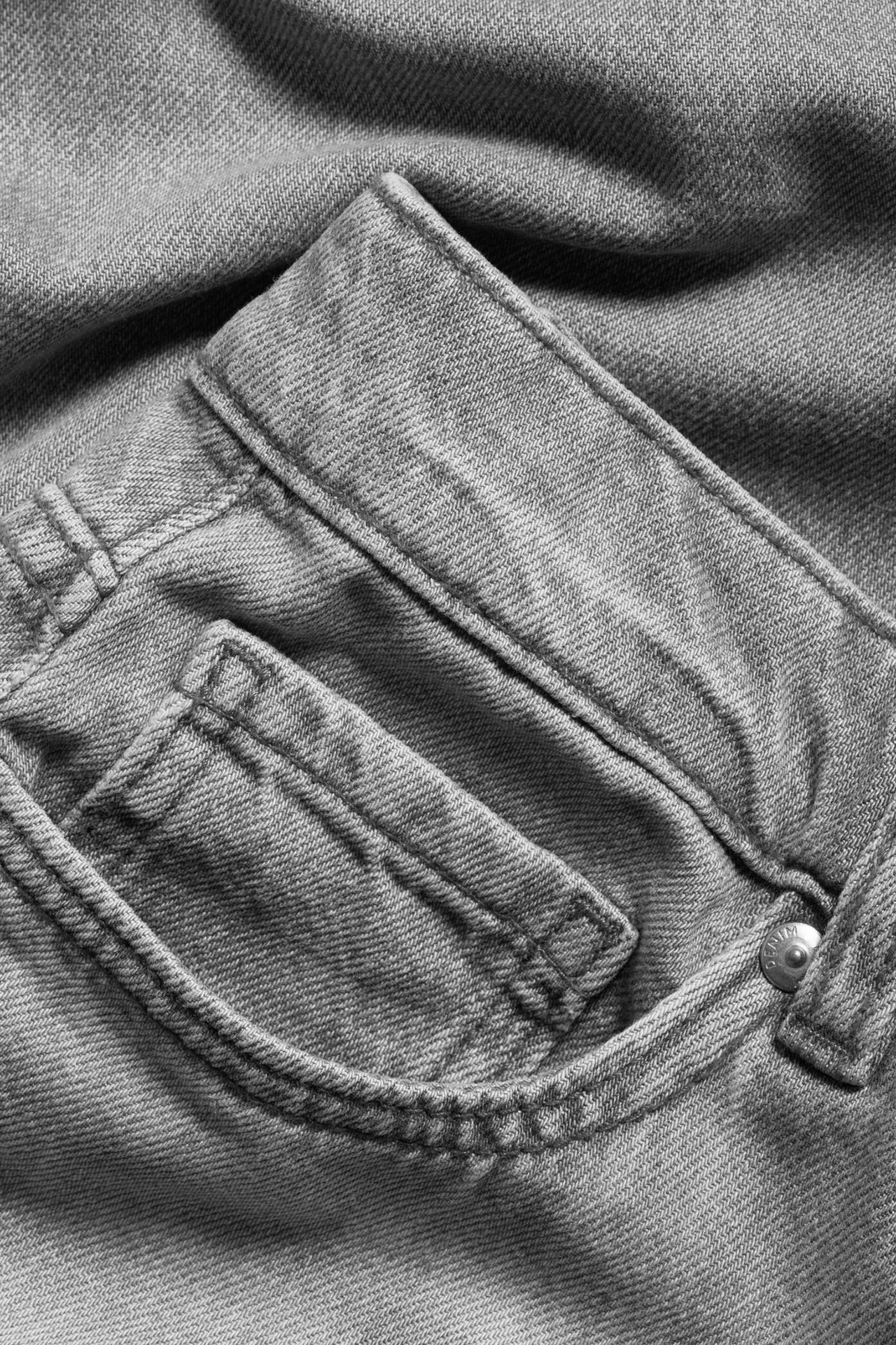 Nærbilde av lysegrå stive denimjeans med høy midje, vide ben, frontlomme og beltehemper.