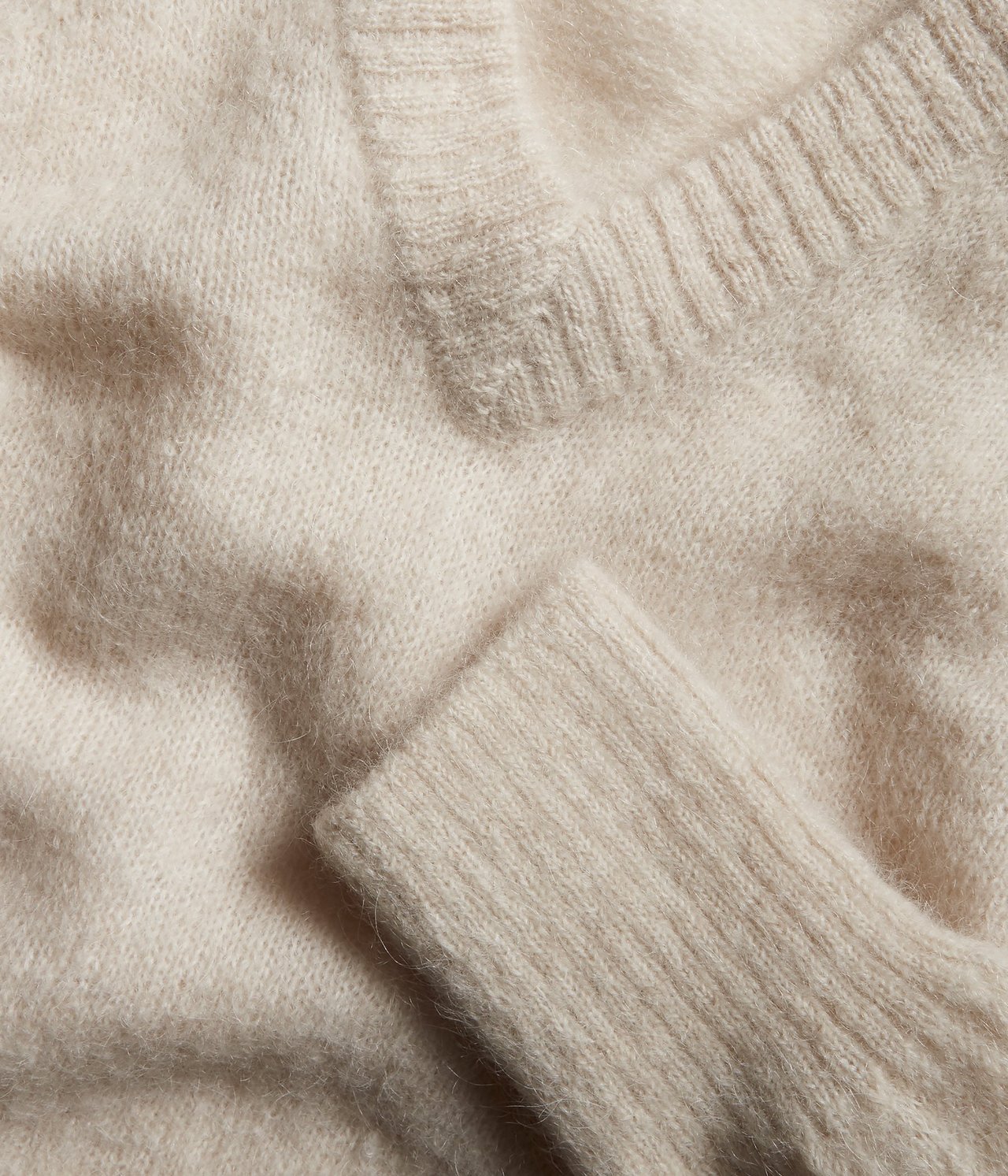 Zbliżenie na jasnobeżowy melanżowy sweter z dzianiny z domieszką wełny, z dekoltem w serek i ściągaczem.