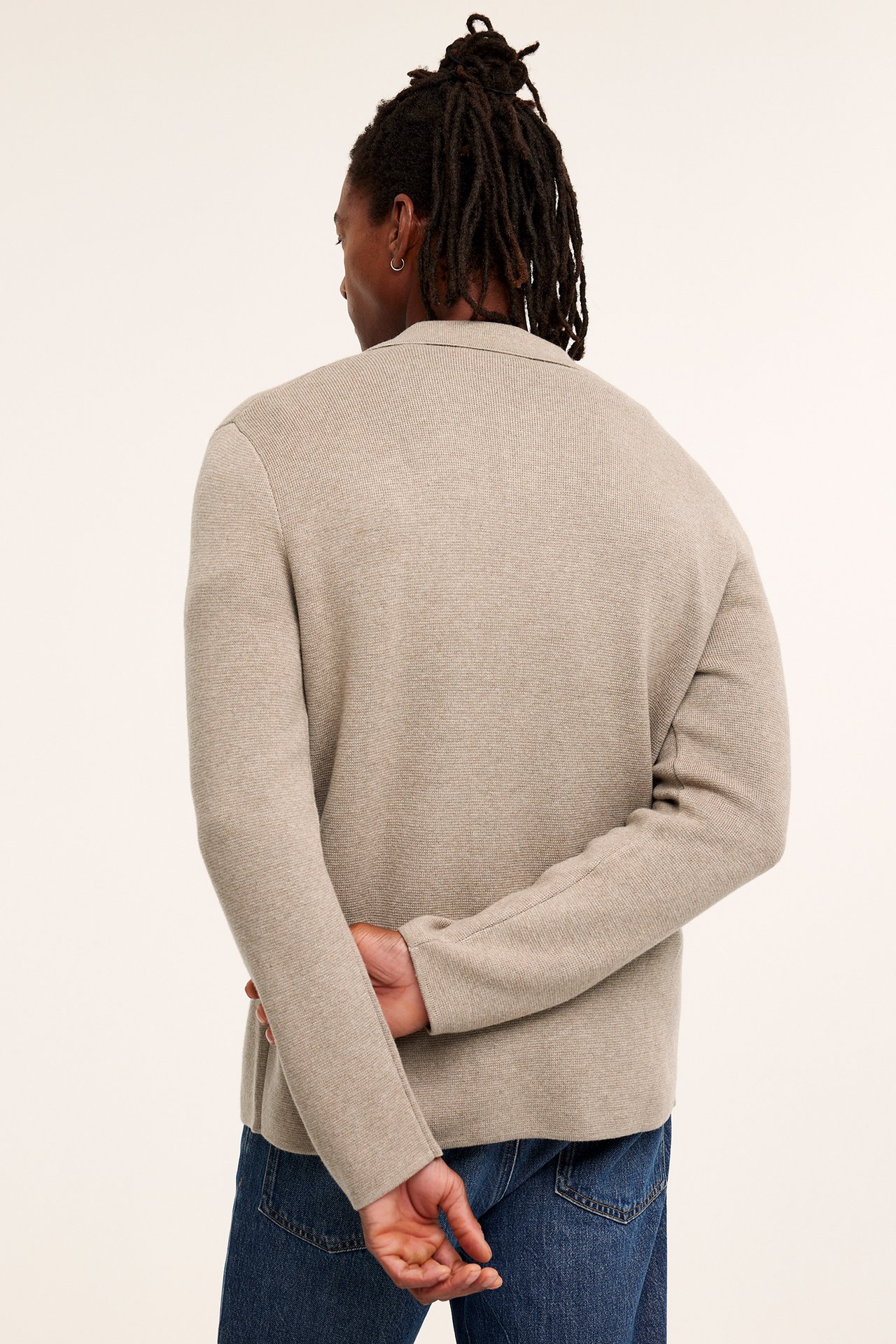 Bakfra av en mann i en melert beige strikket cardigan med krage og blå jeans.