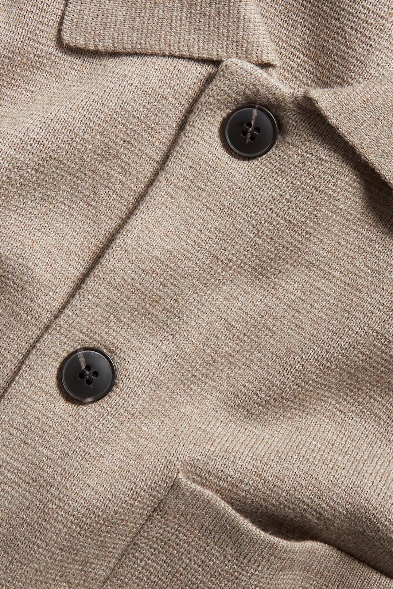 Nærbilde av en melert beige strikket cardigan med krage og mørke knapper foran.