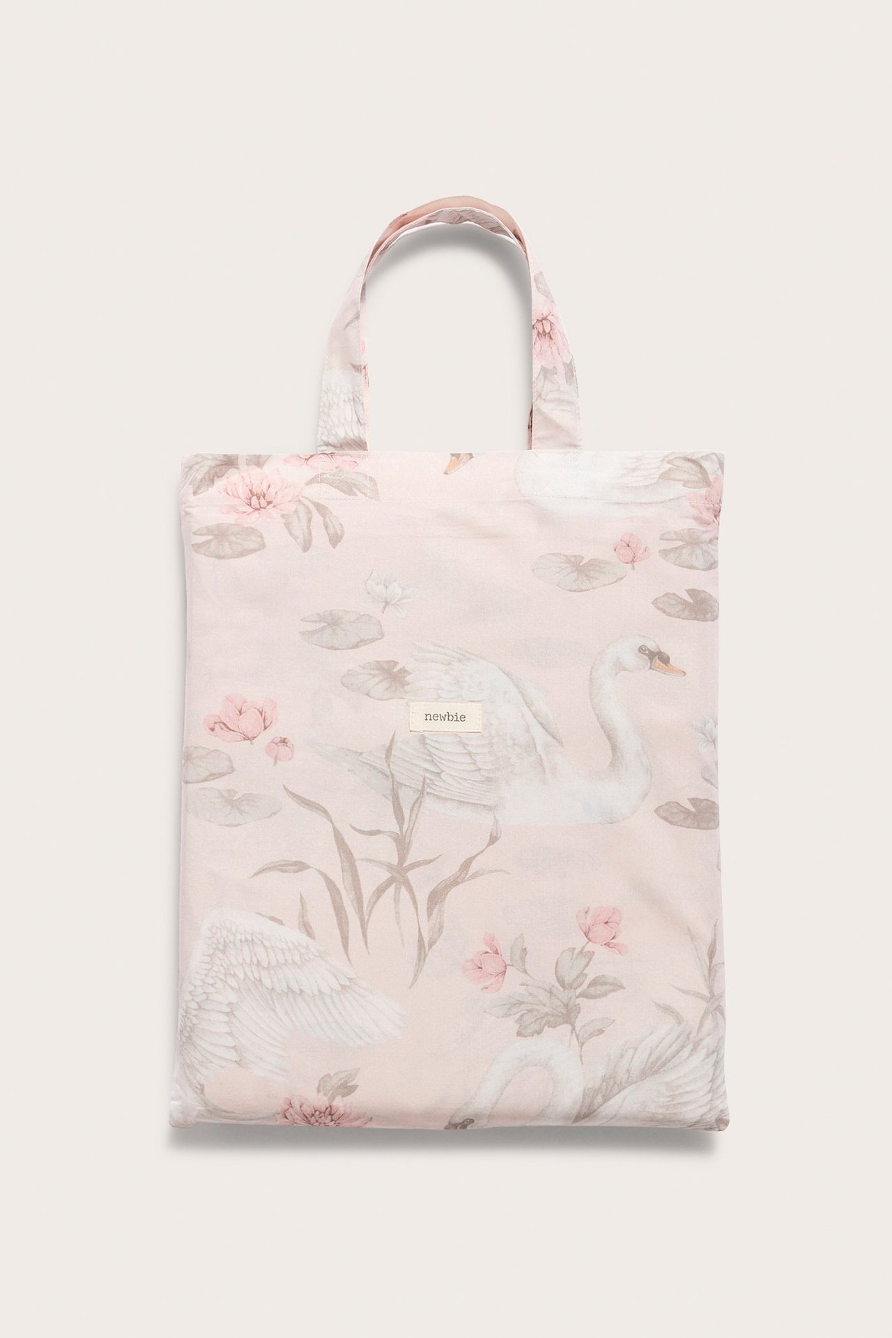 Framifrån: Ljusrosa bäddset i bomull med svan- och blommönster, vikt i matchande tygpåse.