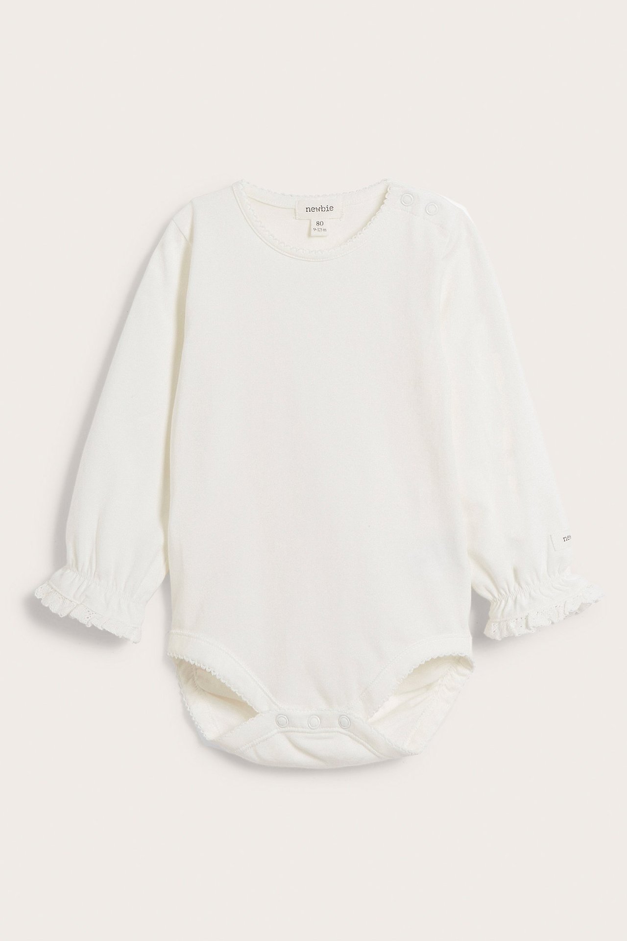 Framsida av en offwhite långärmad babybody med picotkant, tryckknappar och volangärmslut med spets.