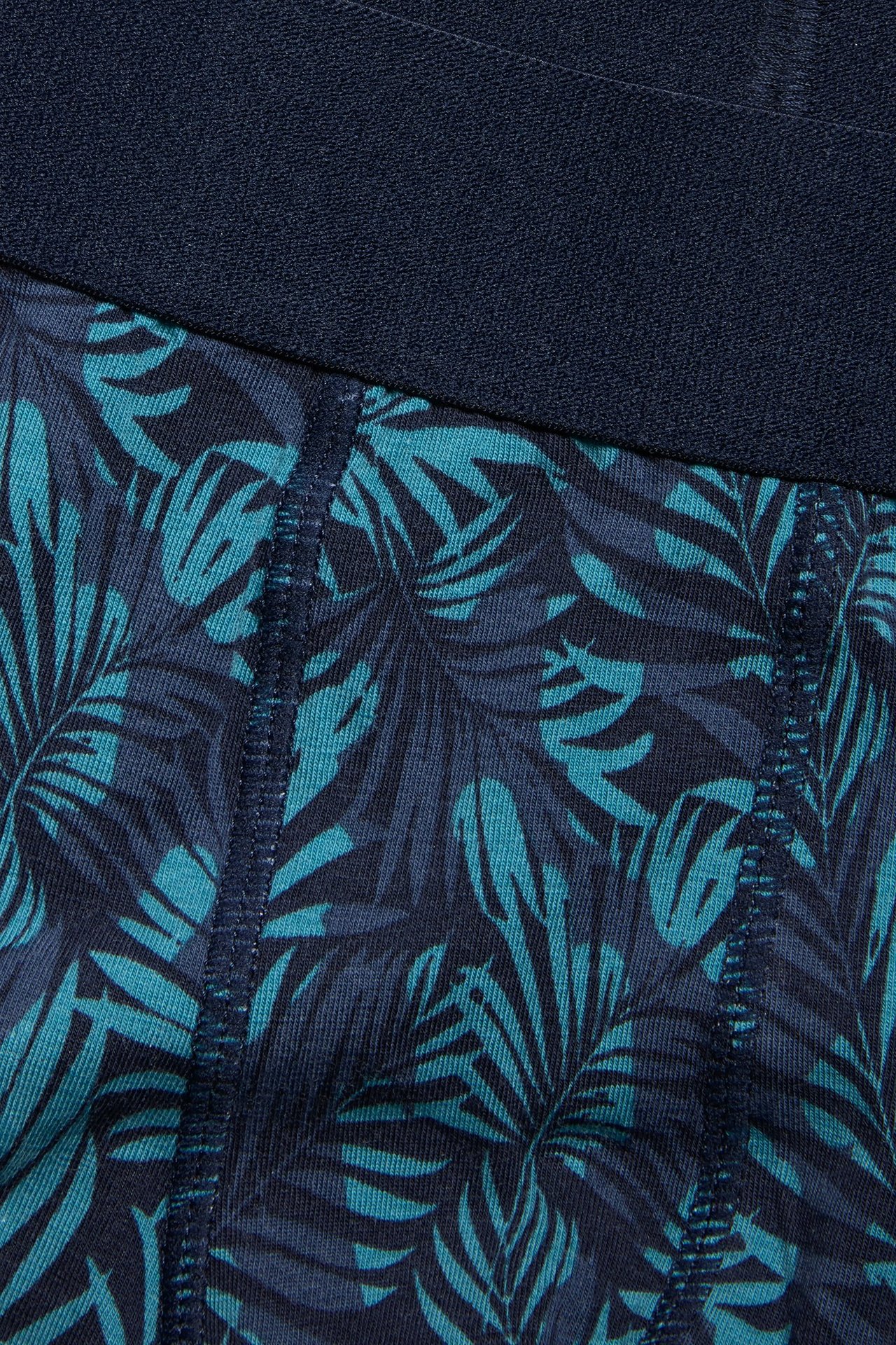 Nærbilde av mønstrede jerseyboksere for menn med mørkeblå elastisk linning og turkis bladtrykk.
