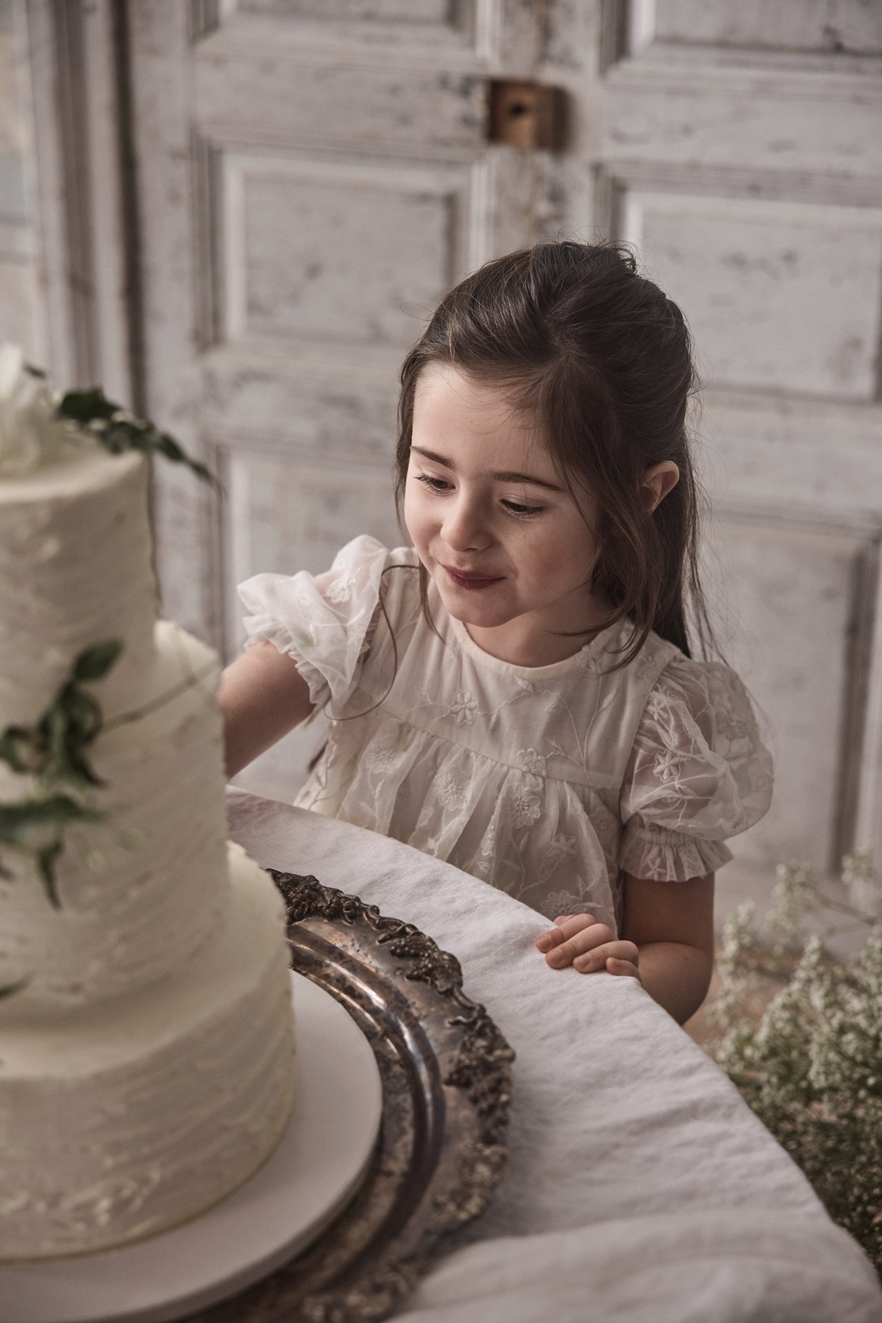 Widok z przodu dziecka w ecru haftowanej sukience z siateczki z bufiastymi rękawami, patrzącego na tort.