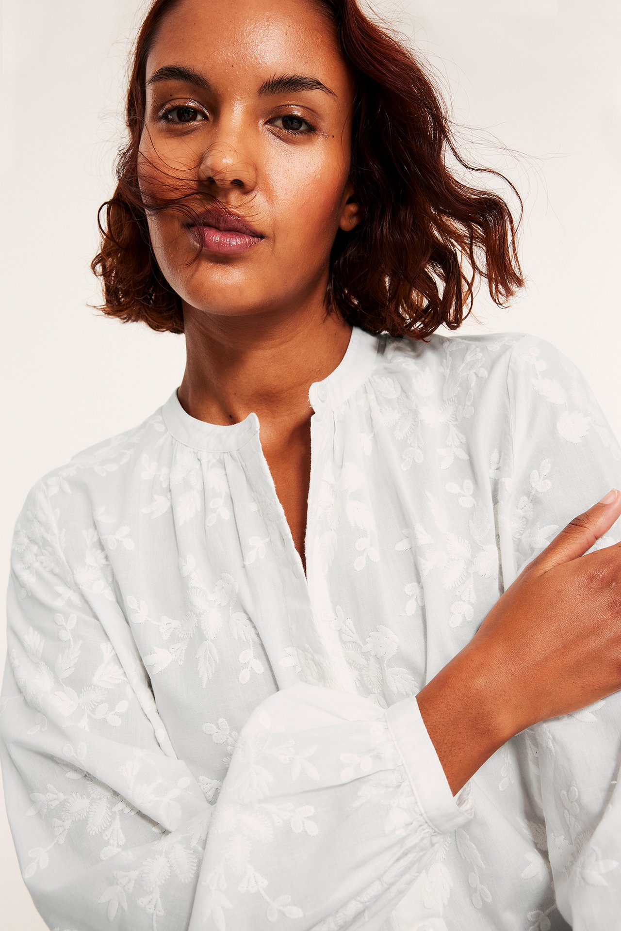 Kvinne i offwhite-bluse med broderte blomster, knapper og løs passform.