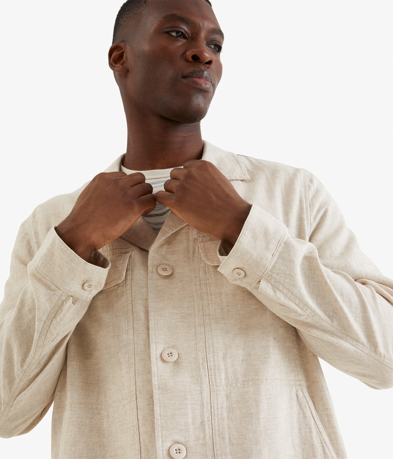 Lähikuva edestä miehestä beigessä pellavasekoitepaitatakissa raidallisen t-paidan päällä.