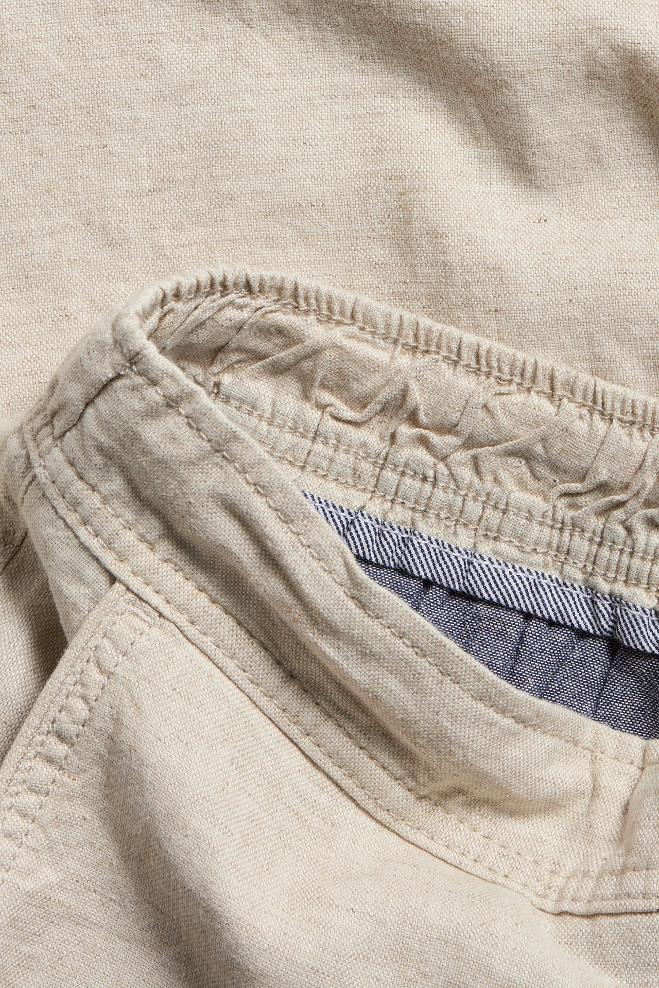 Zbliżenie na jasnobeżowe szorty z mieszanki lnu z elastycznym pasem i pasiastą podszewką.