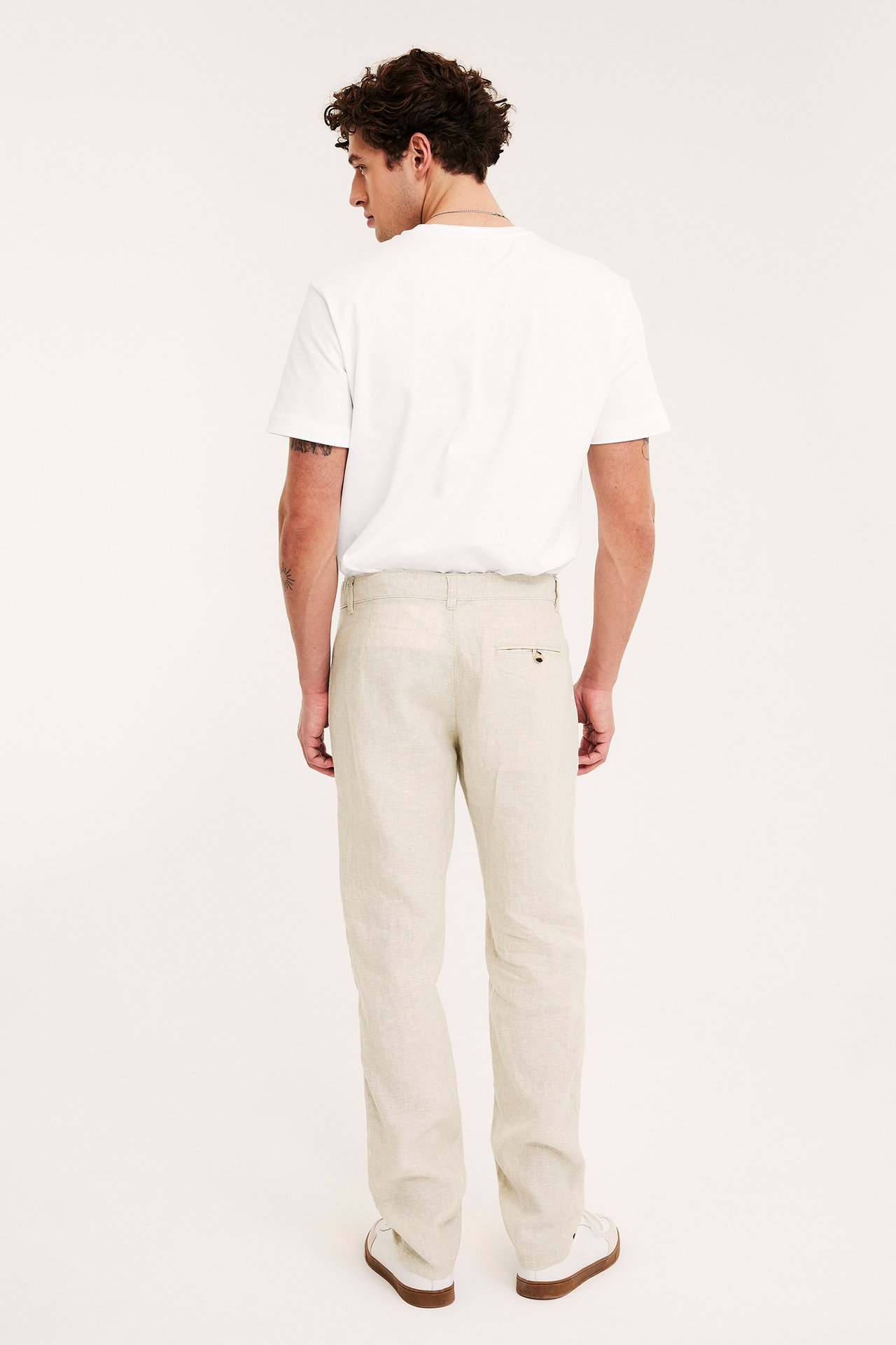 Man bakifrån i ljusa beige linnebyxor, vit t-shirt och vita sneakers.