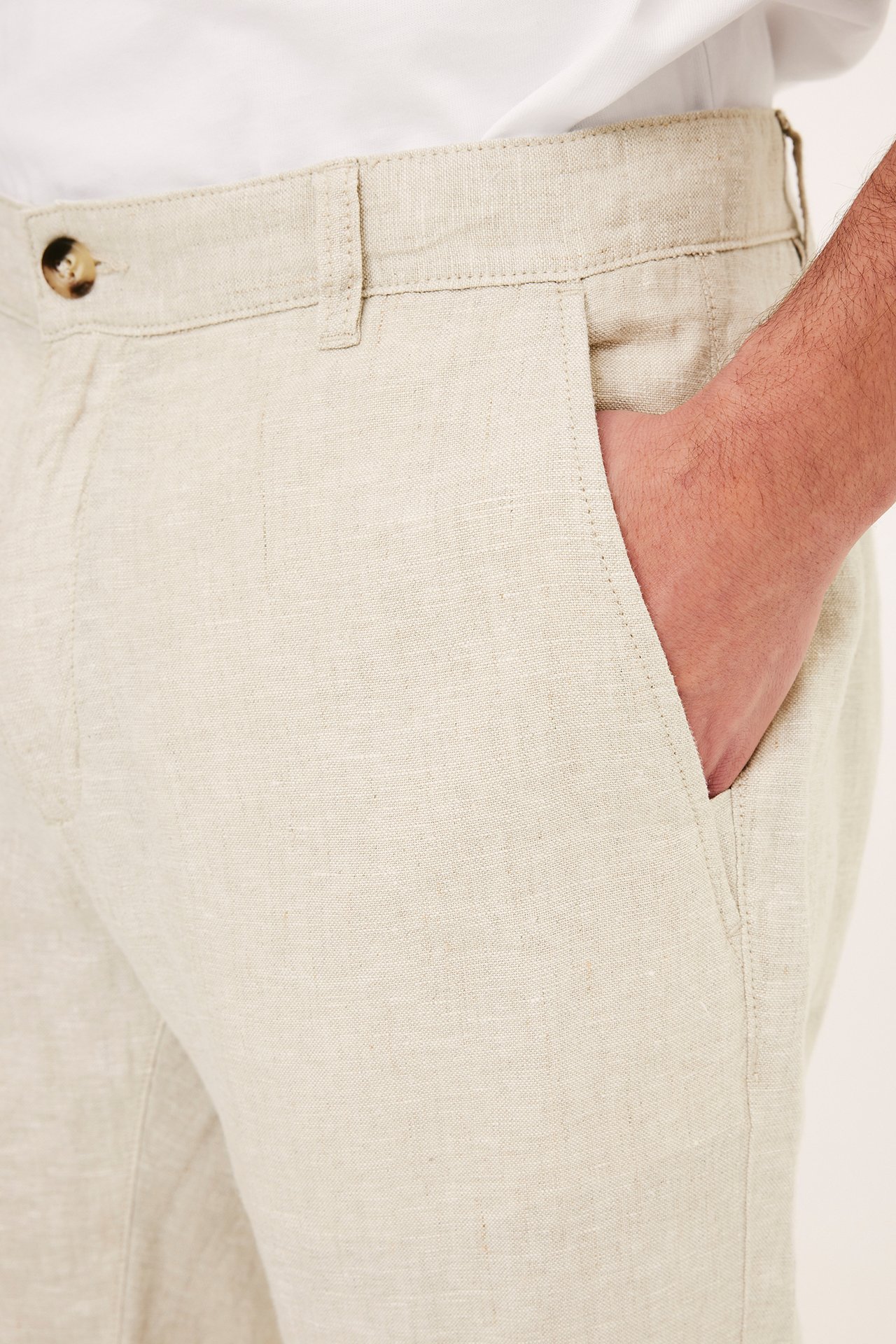 Närbild, sidovy av en man i ljusbeige linnebyxor med brun knapp, handen i fickan.