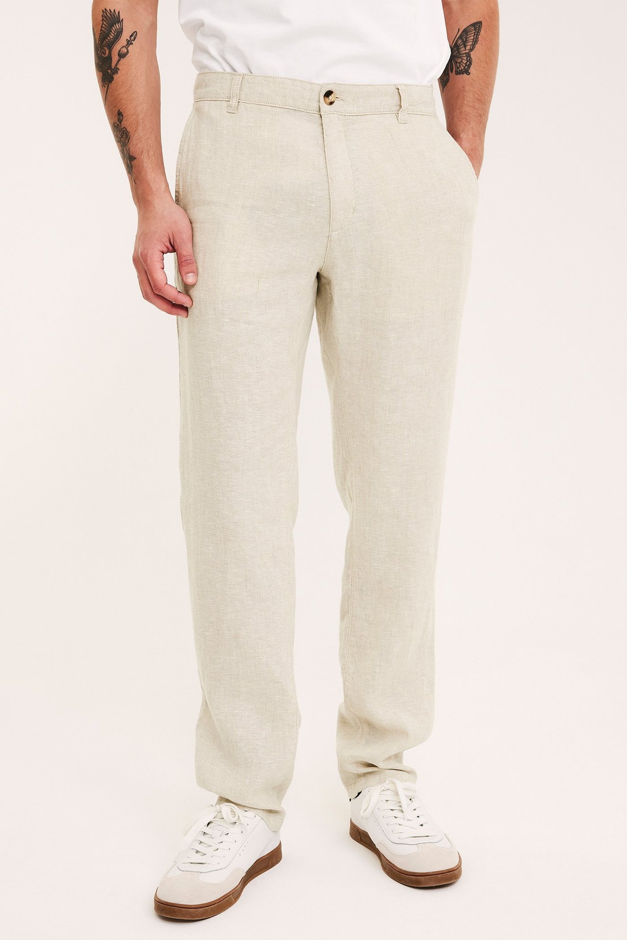Frontvy av man i ljusbeige linnebyxor, vit t-shirt och vita och bruna sneakers.