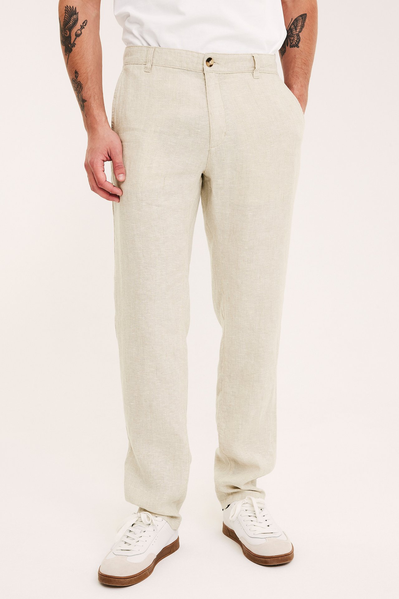 Etunäkymä miehestä yllään vaaleanbeiget pellavahousut, valkoinen t-paita ja valkoiset-ruskeat lenkkarit.