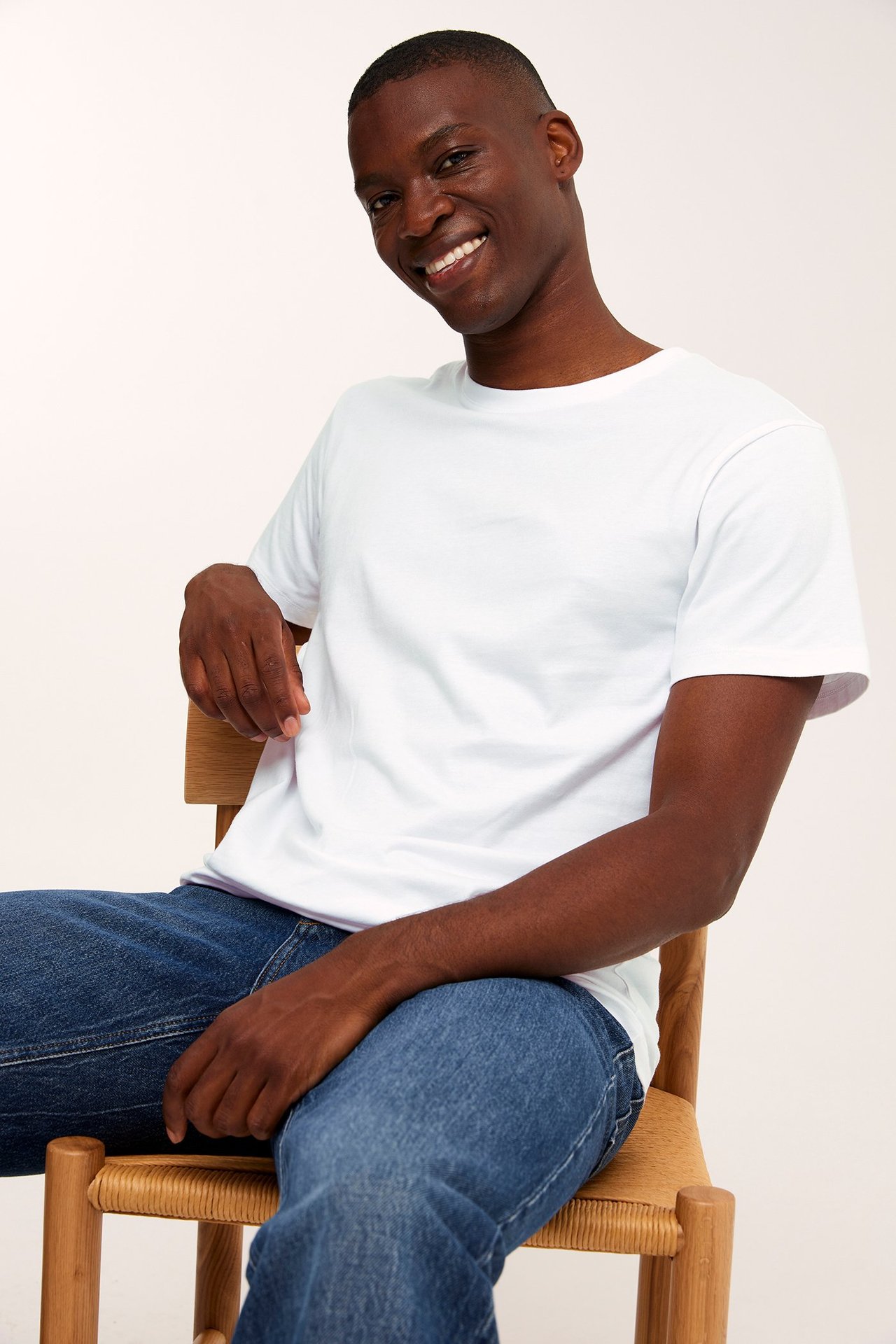 Framifrån, leende man i vit rundhalsad bomulls-t-shirt och blå jeans.