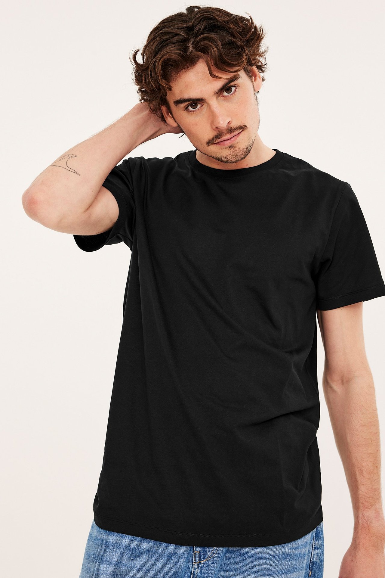 Framifrån, en man i en svart rundhalsad t-shirt i bomull och blå jeans.