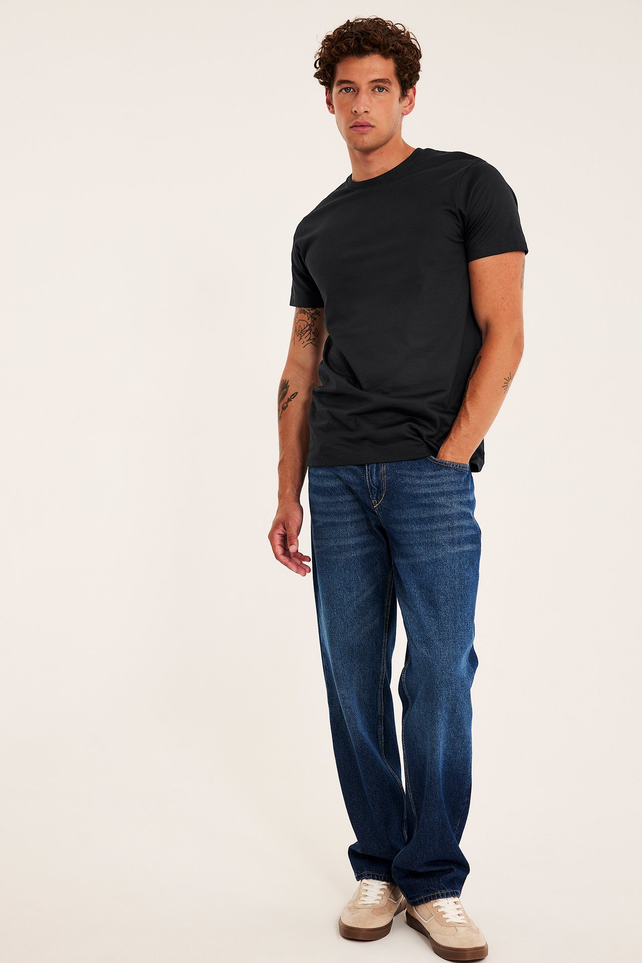 Fremfra, mannlig modell iført svart kortermet t-skjorte, blå rette jeans og beige joggesko.