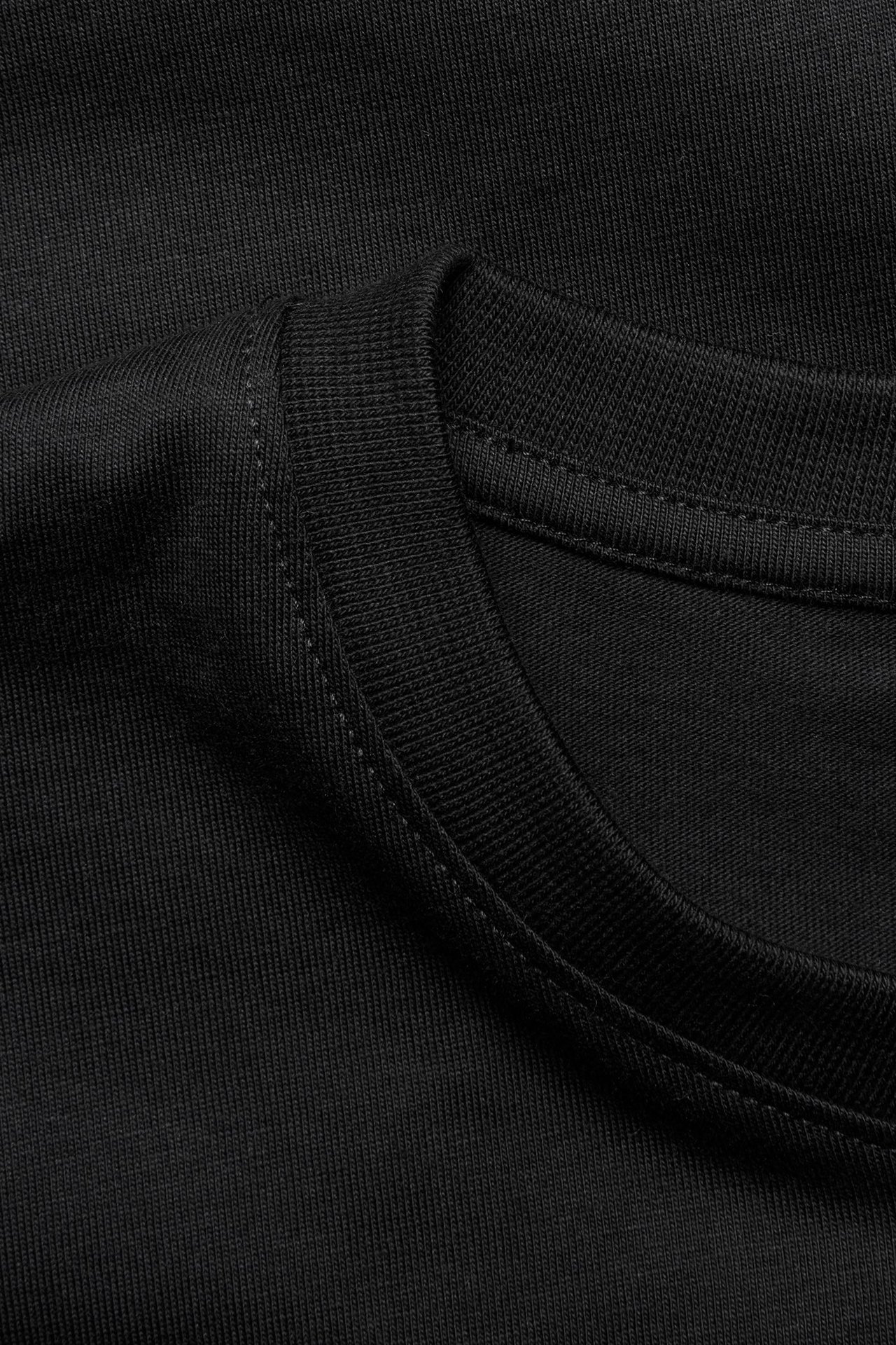 Zbliżenie na czarny, gładki męski t-shirt z okrągłym dekoltem z bawełny, widoczny dekolt i szew na ramieniu.