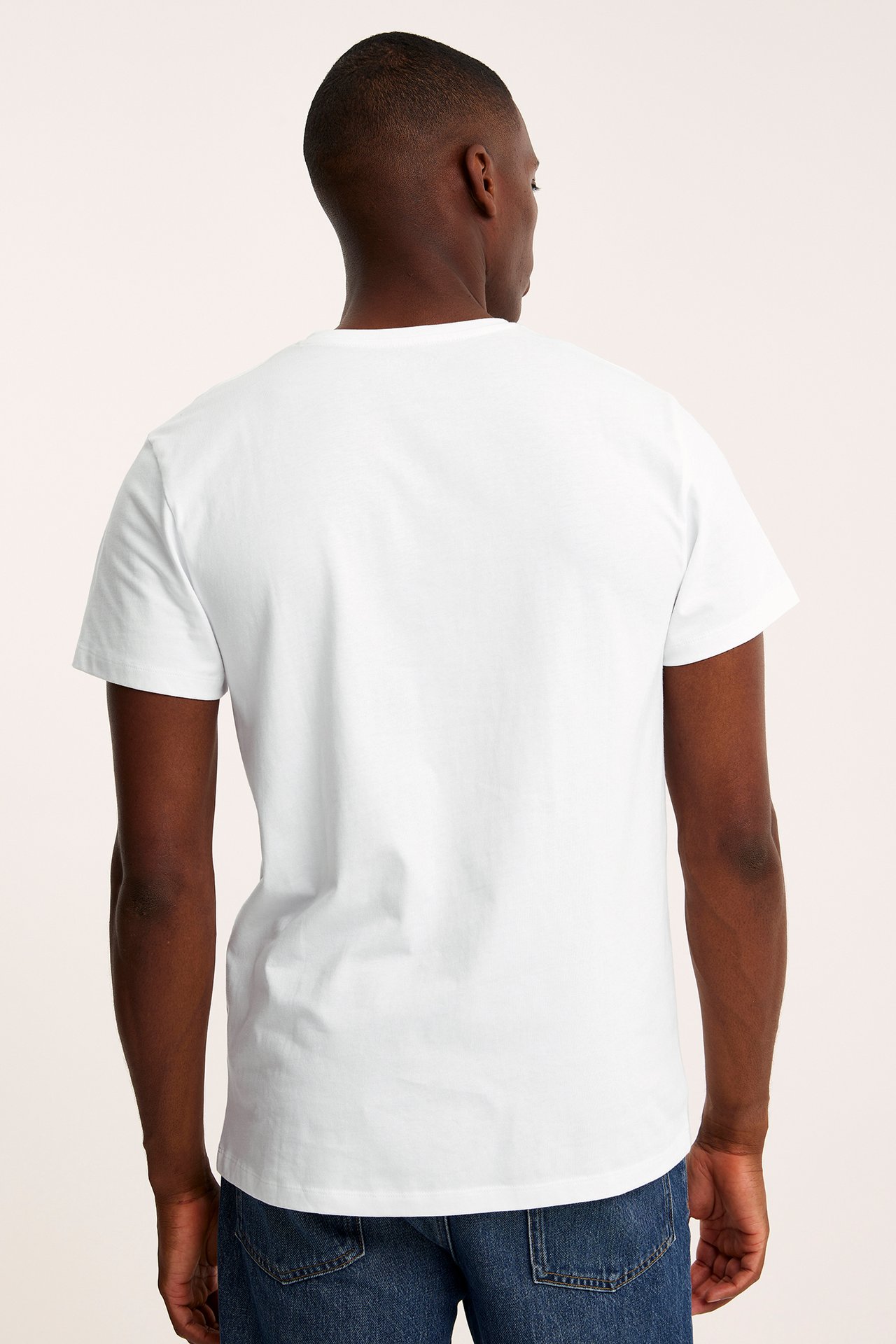 Bakifrån av en man i en enfärgad vit kortärmad t-shirt och blå jeans.