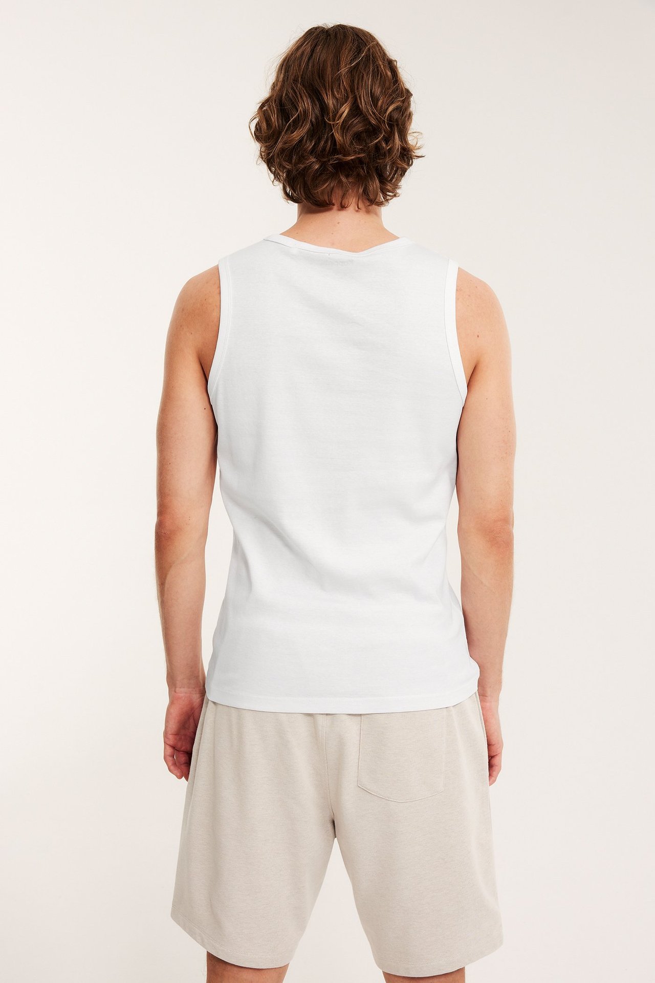 Miehen selkäpuoli valkoisessa ribbineuleisessa puuvillatopissa ja beigessä shortsissa.